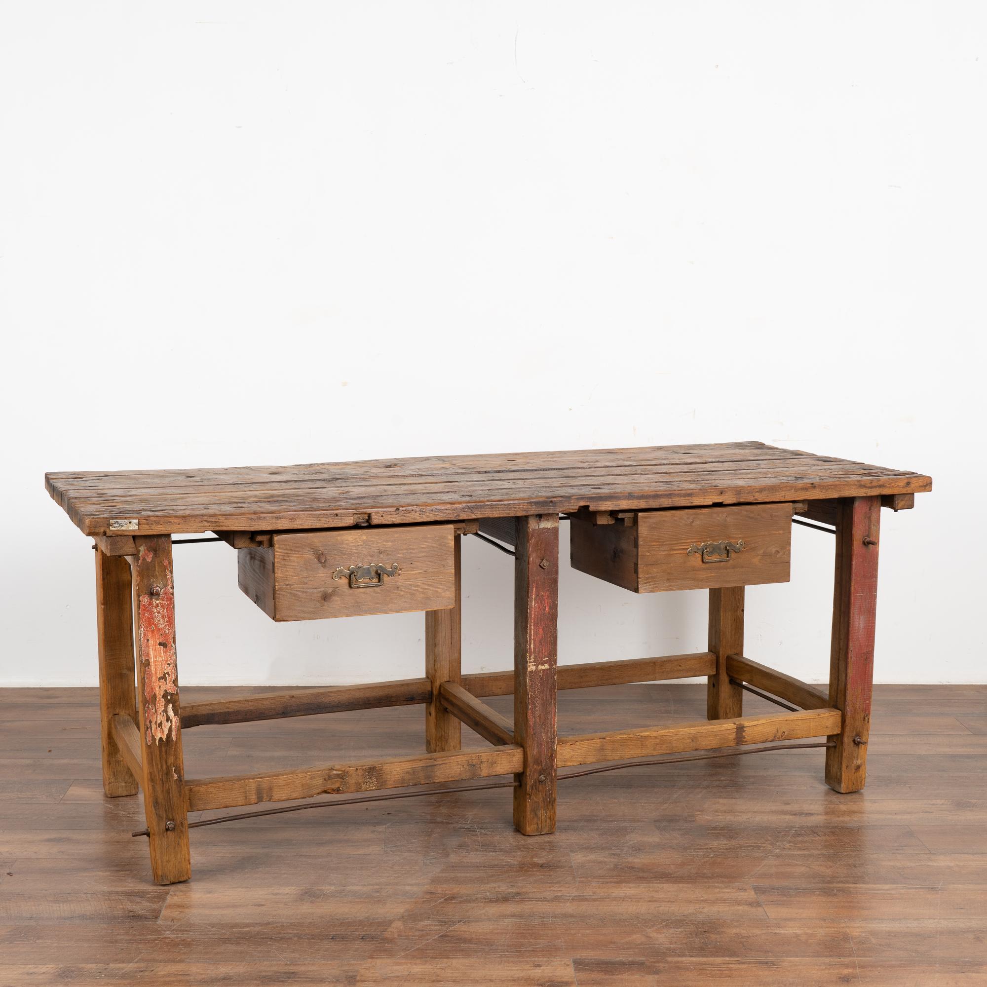 Rustic work table or shop counter with two drawers and residual red paint remaining on legs.
This heavily used table reflects generations of use in every gouge, nick, scratch, hole and stain. Typical aged separation of planks.
Metal rods add an