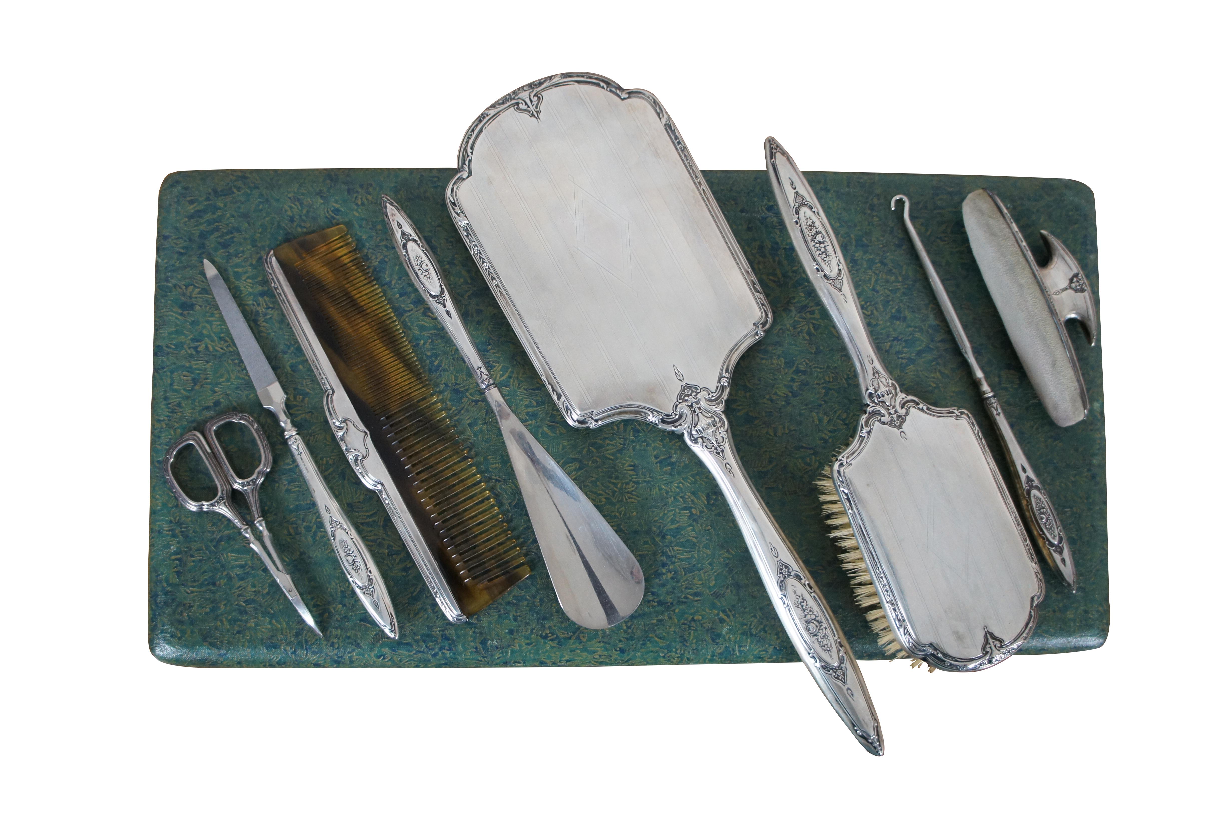 Impressive antique eight piece vanity grooming set by Robert Wallace & Sons featuring Art Deco styling with floral motif.  Includes mirror, brush, comb, scissors, file, button hook loop, buffing pad, shoe horn and purple velvet lined box case.

