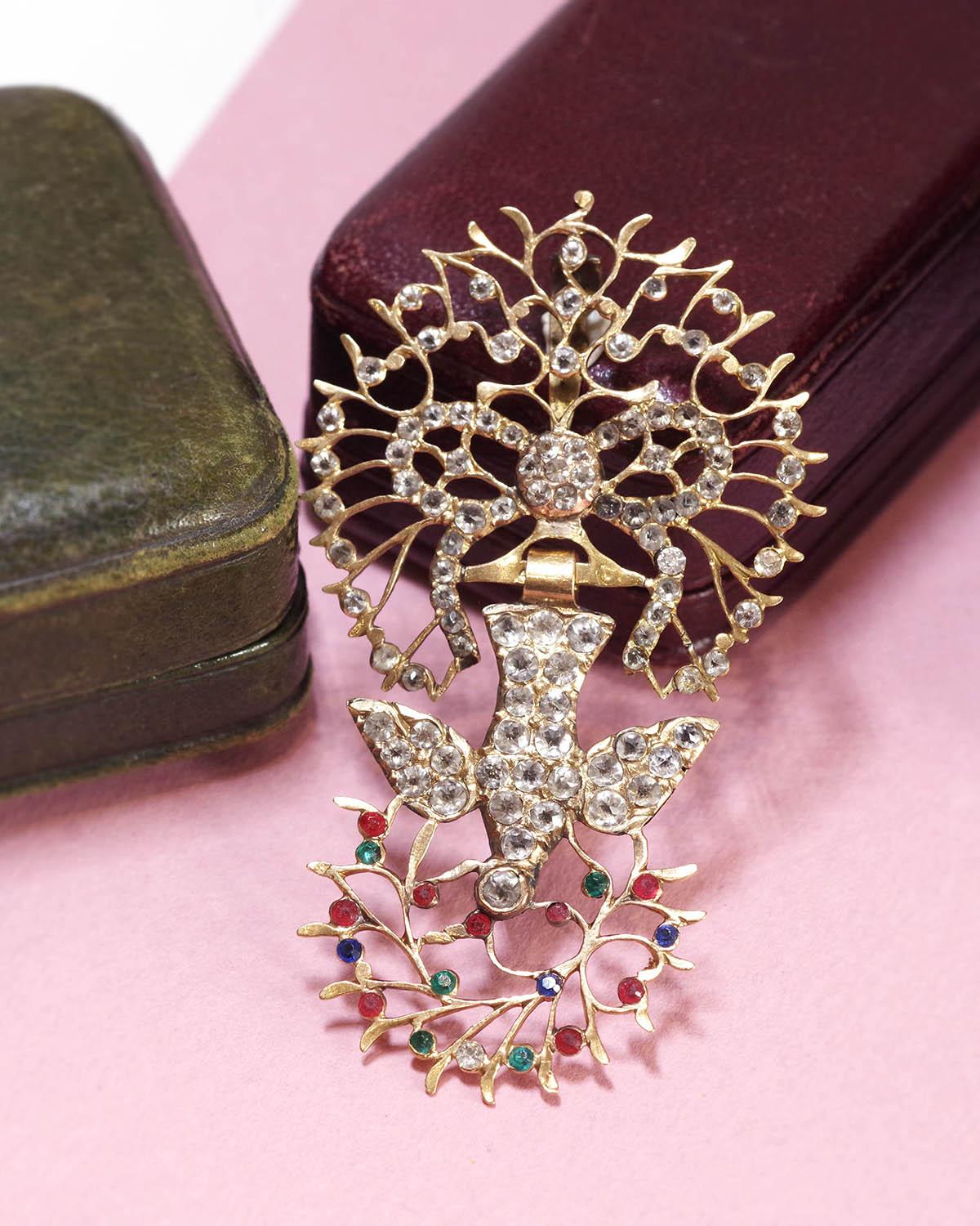 Antique Saint Esprit pendant in 18 karat gold. Originally from Normandy, it features a dove with its head down, holding an olive branch in its beak. The bird hangs from a bow richly decorated with white paste stones, imitating diamonds. Red and