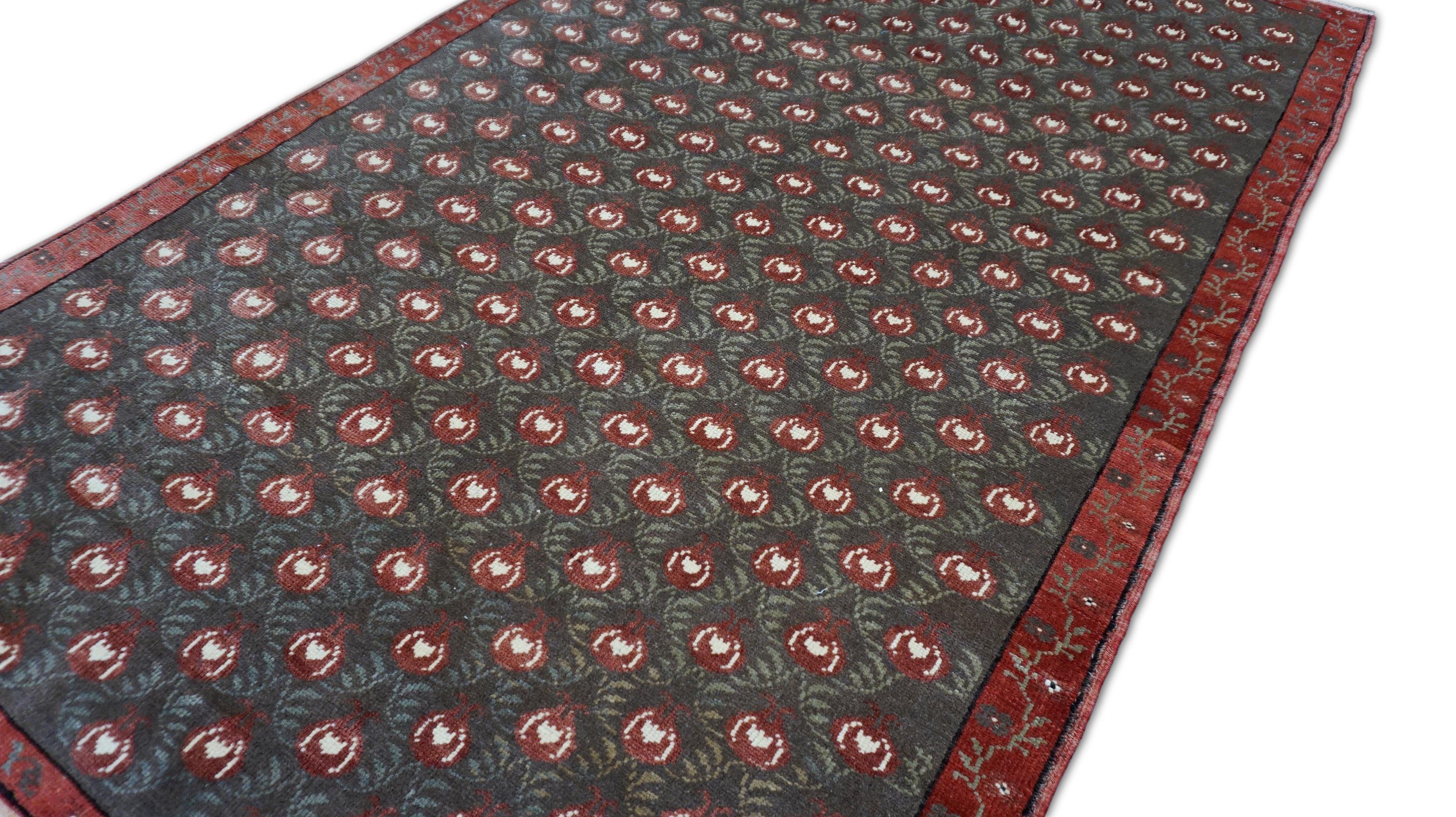 Questo tappeto vintage in lana annodato a mano è un esempio straordinario di design simbolico e di meticolosa lavorazione artigianale. Il campo verde oliva è riccamente ornato da un motivo ripetuto rosso e nero - un antico simbolo di fertilità,