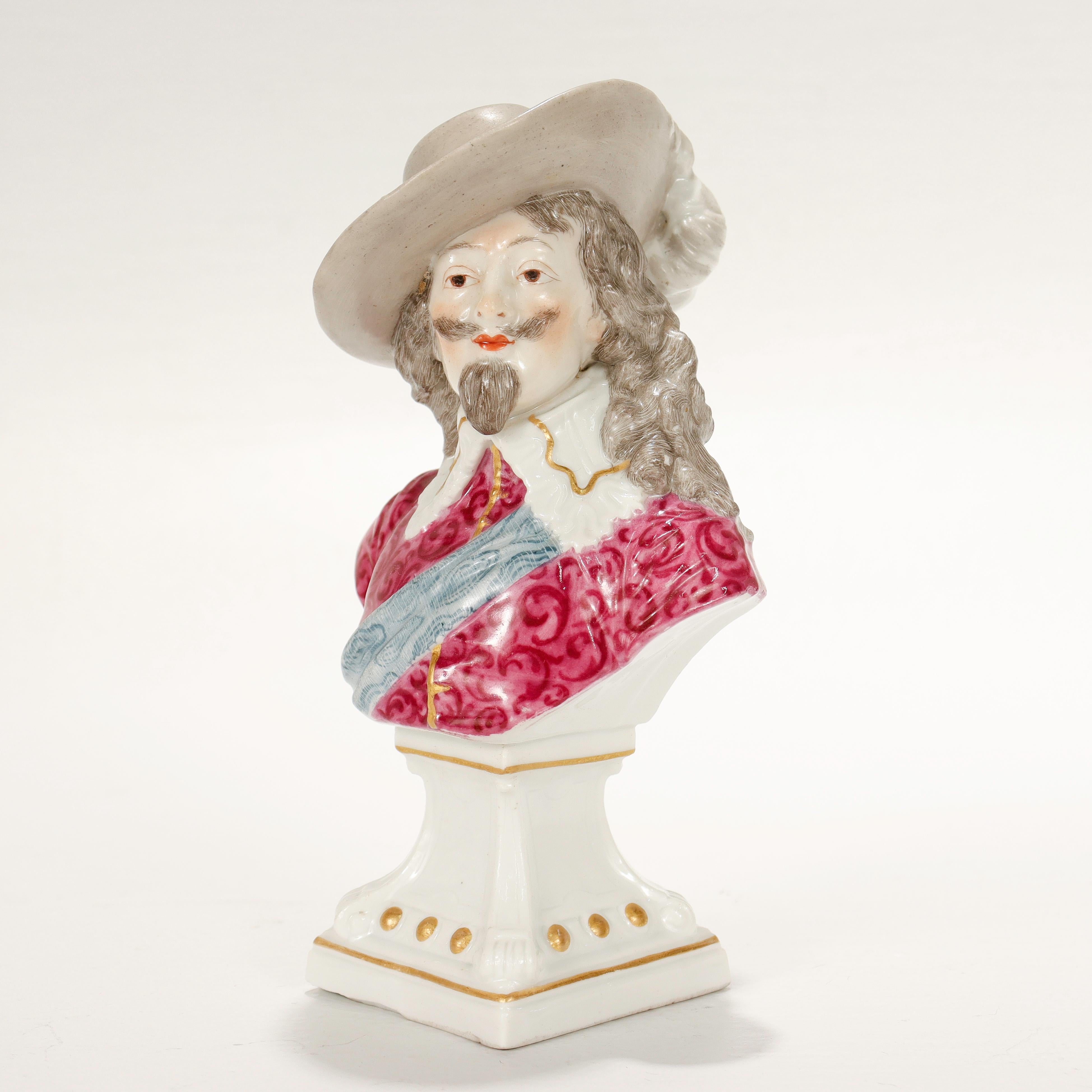 Una bella statuetta o busto di porcellana antica.

Di Samson & Cie.

A forma di busto di un uomo vestito in modo variopinto con un colletto a balze e un cappello con piume. 

Posizionato su un basamento bianco con riflessi dorati.

Sul retro dello