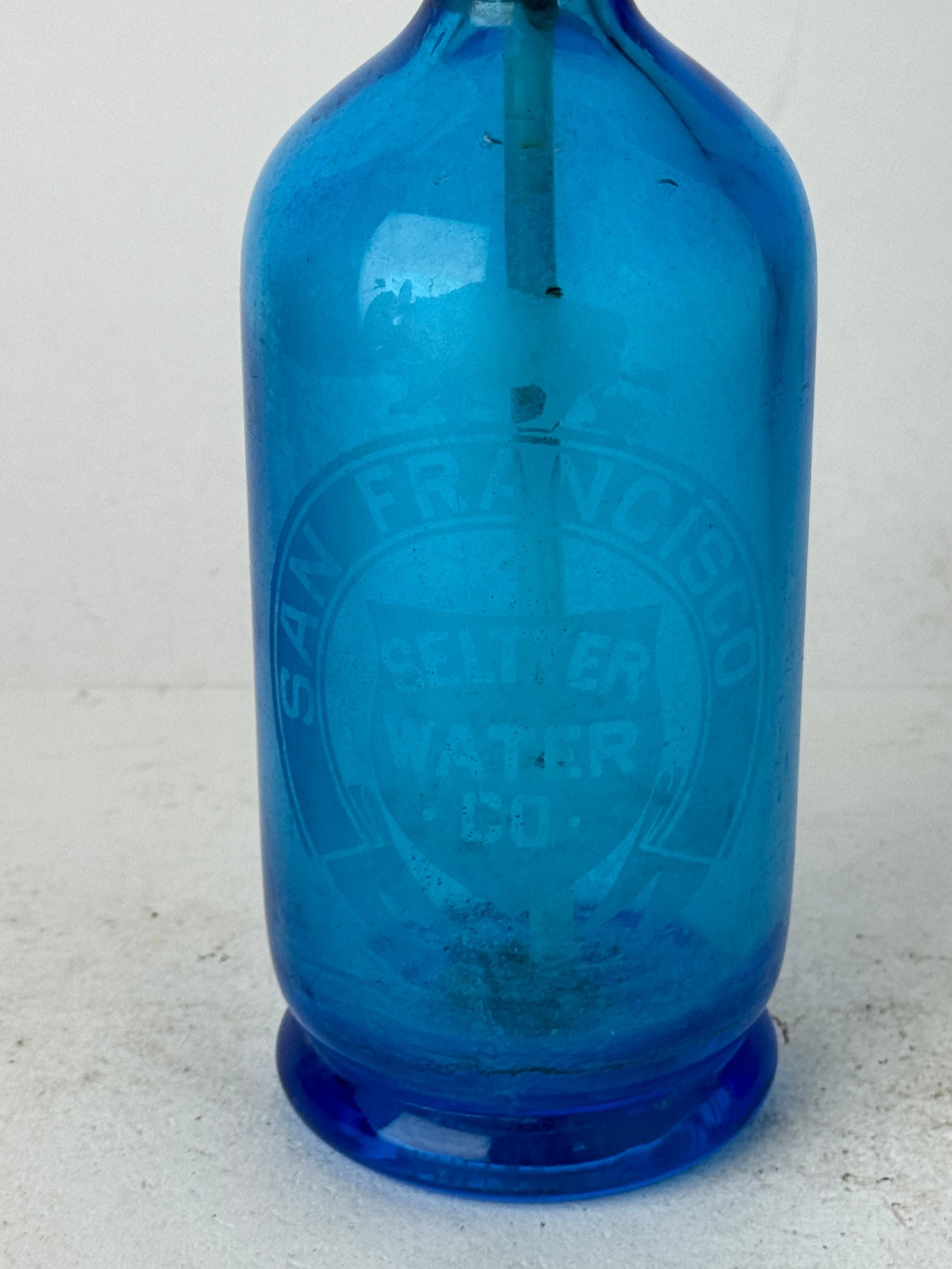 Ajoutez une touche de charme ancien à votre bar ou à votre étalage avec notre captivante bouteille d'eau de Seltz en verre bleu antique/vintage, fabriquée en Autriche pour la prestigieuse San Francisco Seltzer Water Company. Cette pièce étonnante ne