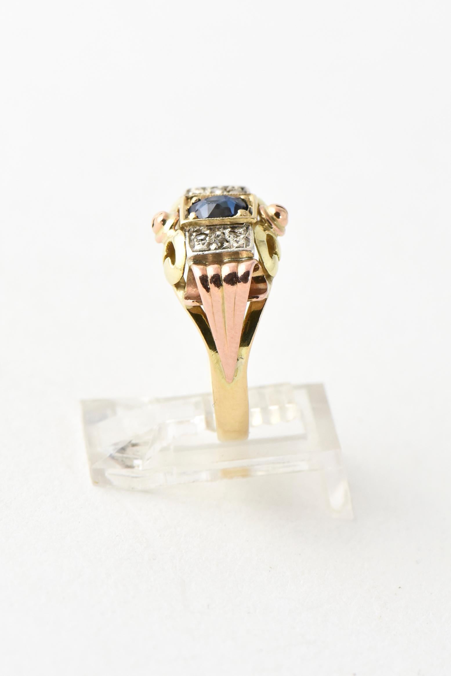 Antique 14K rose, yellow, and white gold ring with ribbed scroll sides featuring a sapphire center stone accented by three diamonds on each side. Marked: 585. Size: 7; can be sized. Abrasions on sapphire, age wear.
