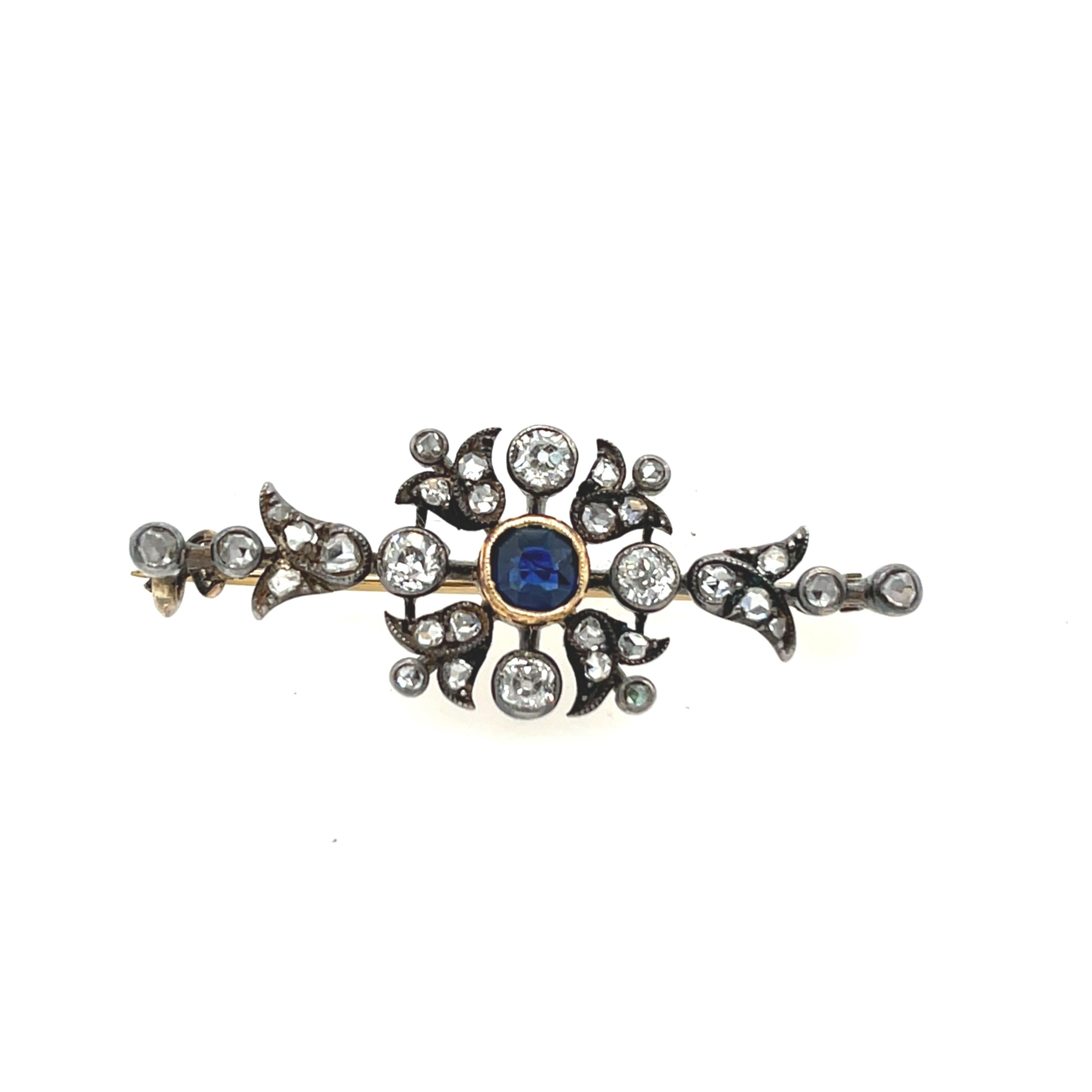 Eine bezaubernde antike Brosche mit einem leuchtenden Saphir in der Mitte, der durch Diamanten im Rosenschliff wunderbar ergänzt wird. 
Das filigrane Design ist aus 14 Karat Weißgold und Silber gefertigt und verbindet Eleganz mit Vintage-Charme.