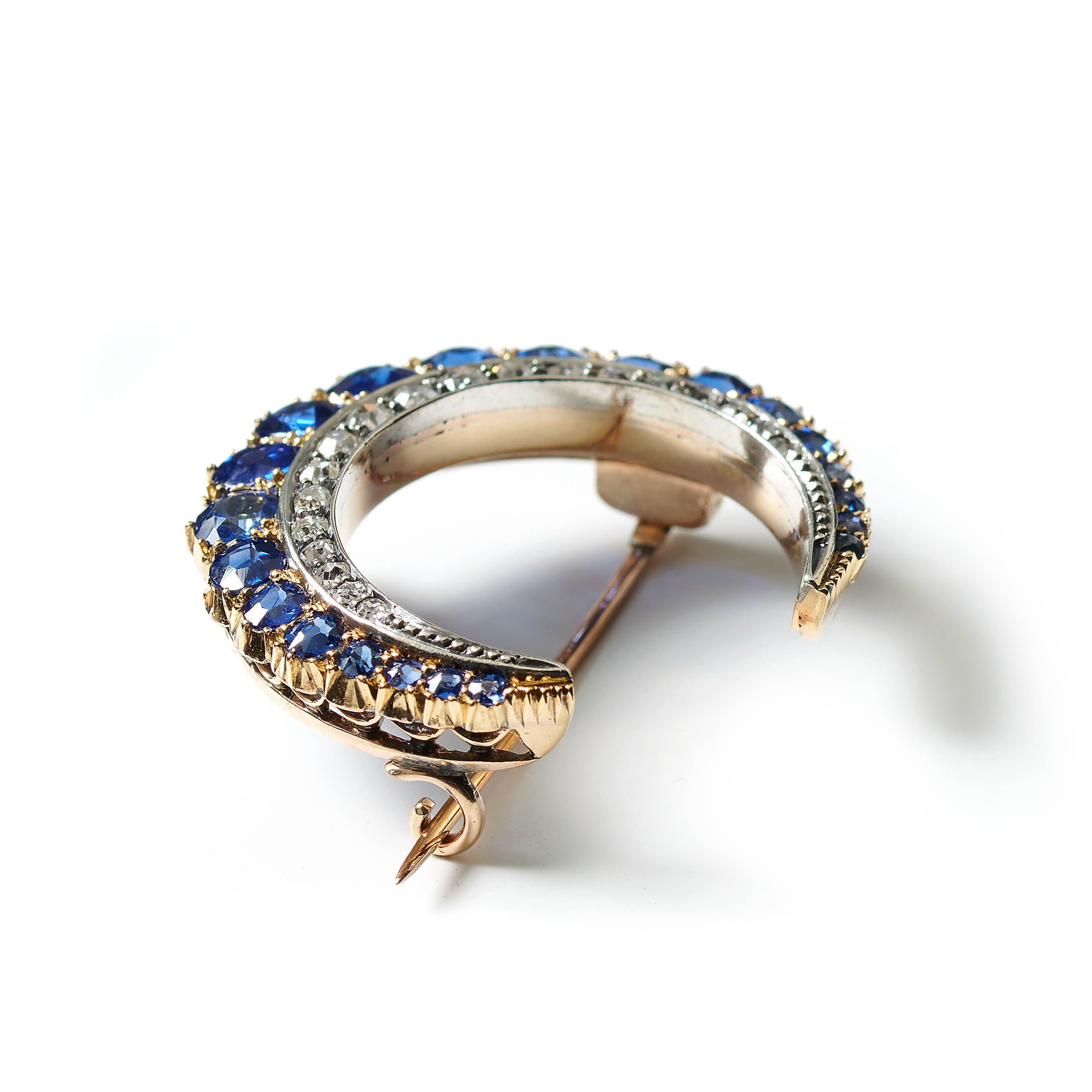 An antique sapphire and diamond crescent brooch, with an outer row of oval and cushion faceted sapphires, graduating from the centre, set in gold, in grains and cut down settings on the outer edge and a gold pierced gallery below, with an inner row