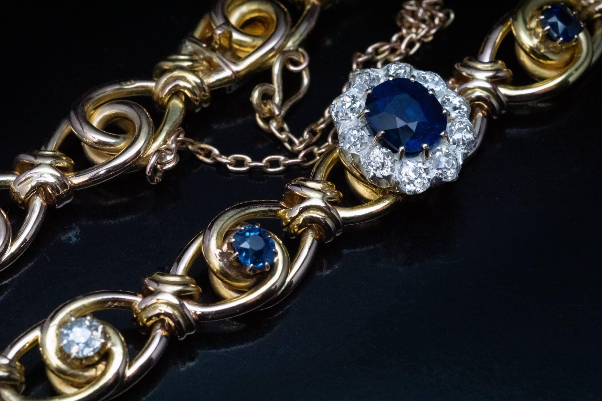 Circa 1890s  The 14K yellow gold link bracelet is centered with a midnight blue sapphire surrounded by sparkling old mine cut diamonds (set in silver over gold). The sapphire and diamond cluster is flanked by two small sapphires and two diamonds. 
