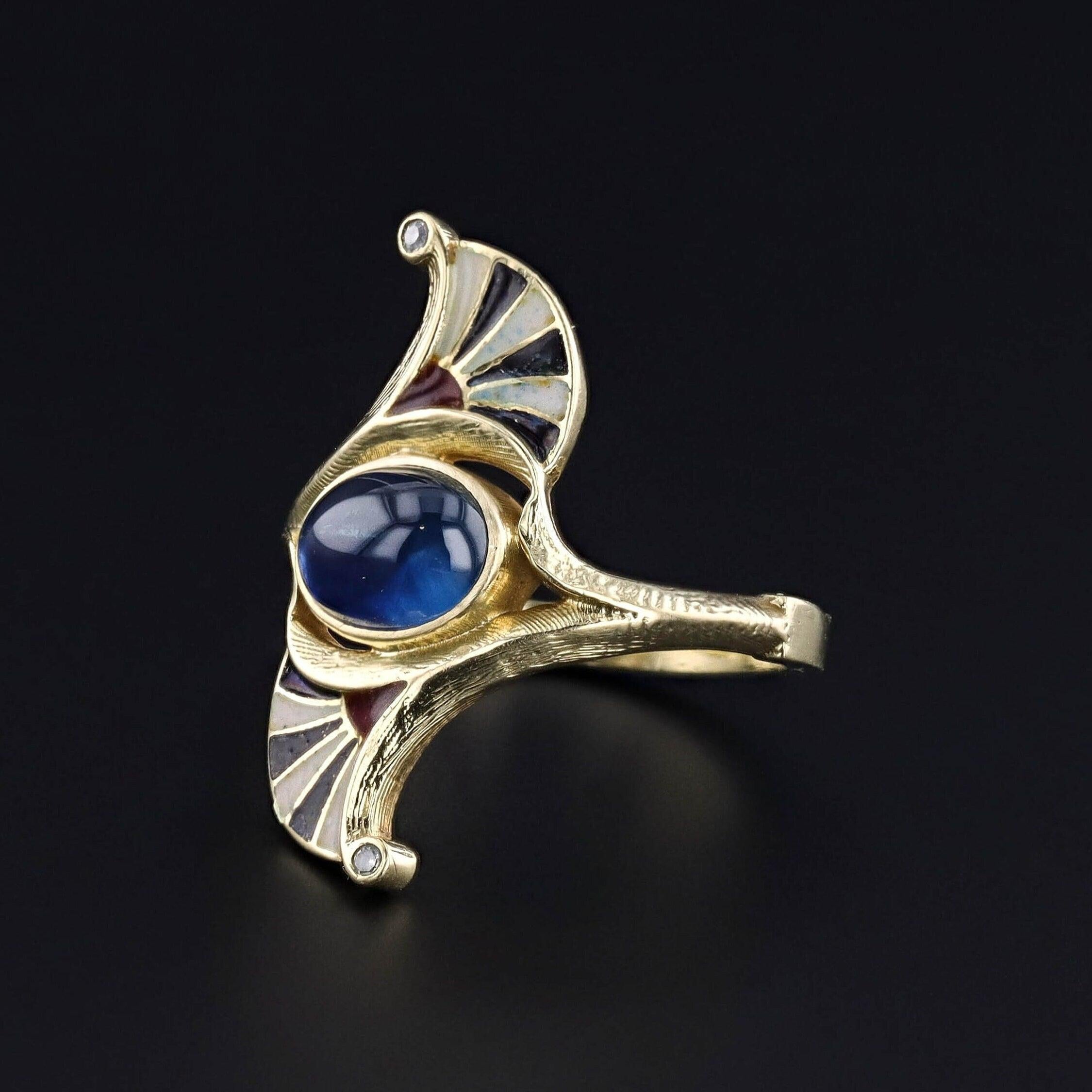 A striking Egyptian Revival ring (circa 1910) with black white and red enamel and a natural blue sapphire at its center. Two tiny diamonds add a glittery flourish on each point of the ring. 

The sapphire cabochon is moderate blue in color and