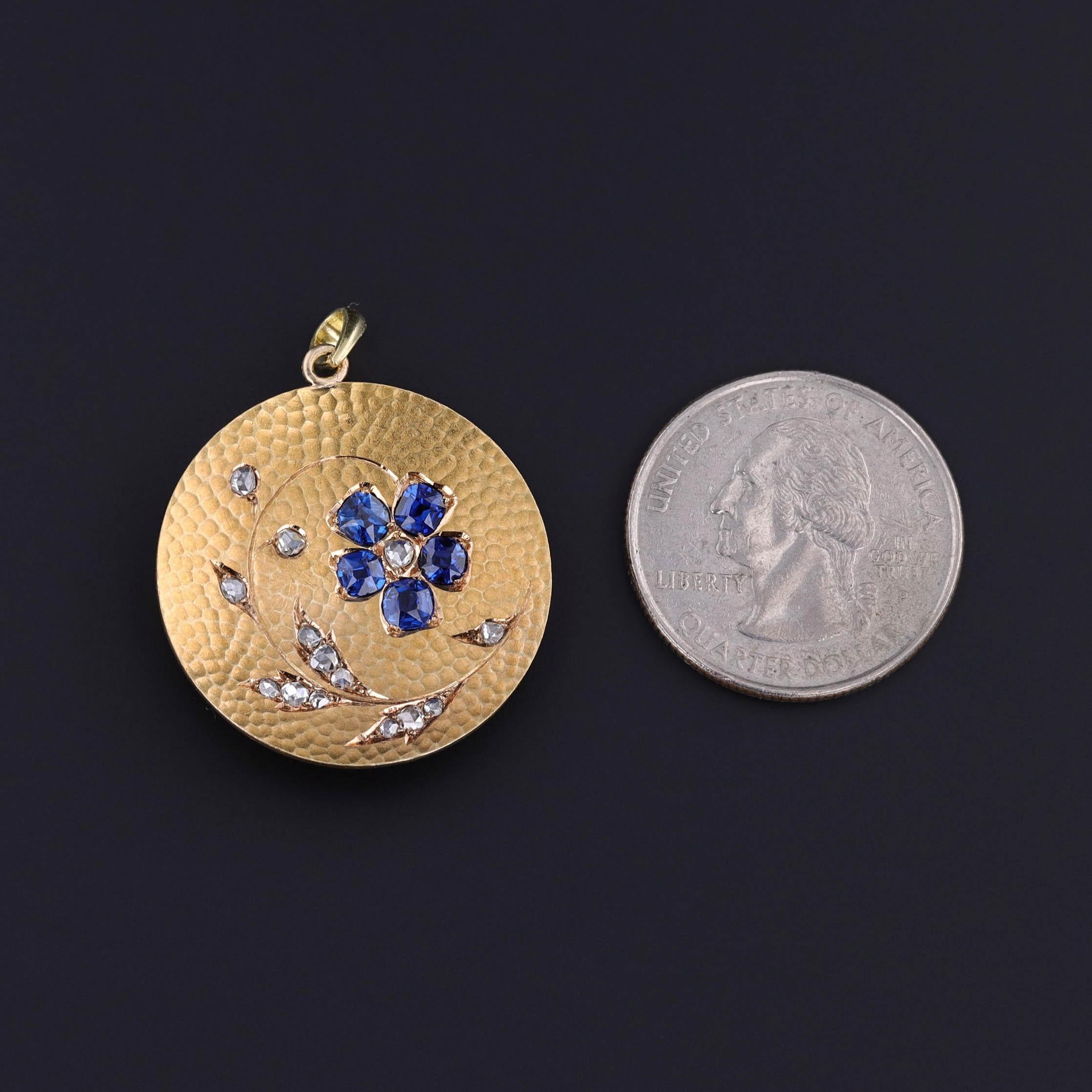 This Art Nouveau pendant (circa 1890-1910) features a hammered 18k bloomed gold surface adorned with a floral motif. At its center, five vibrant natural blue sapphires form a flower with a rose cut diamond center, surrounded by delicate rose-cut
