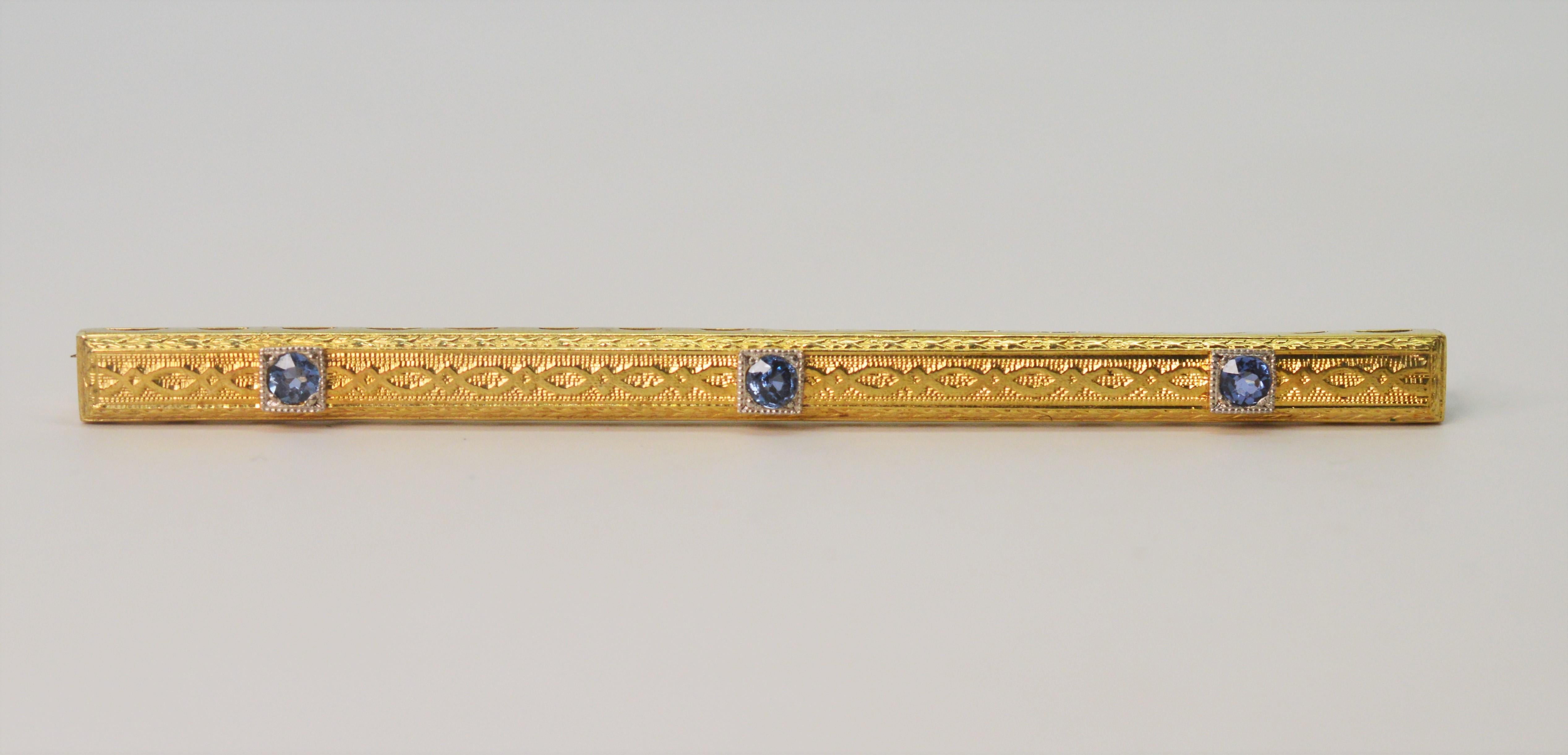 Three round-cut blue sapphires adorn this fancy fourteen carat yellow gold bar pin brooch. Measuring 2-1/2 inches in length, this bar pin brooch has a meandering decorative design that gives it dimension.
  