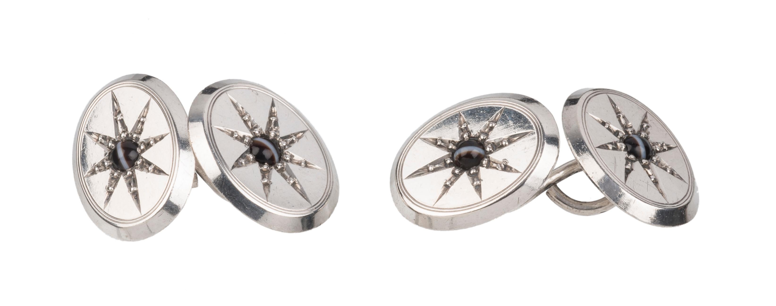Each cufflink consists of two silver oval plaques that are connected by an s-shaped silver hook. The oval segments are embellished with an eight-pointed star framed by a double engraved oval line. Every star holds a banded agate. It's rays are