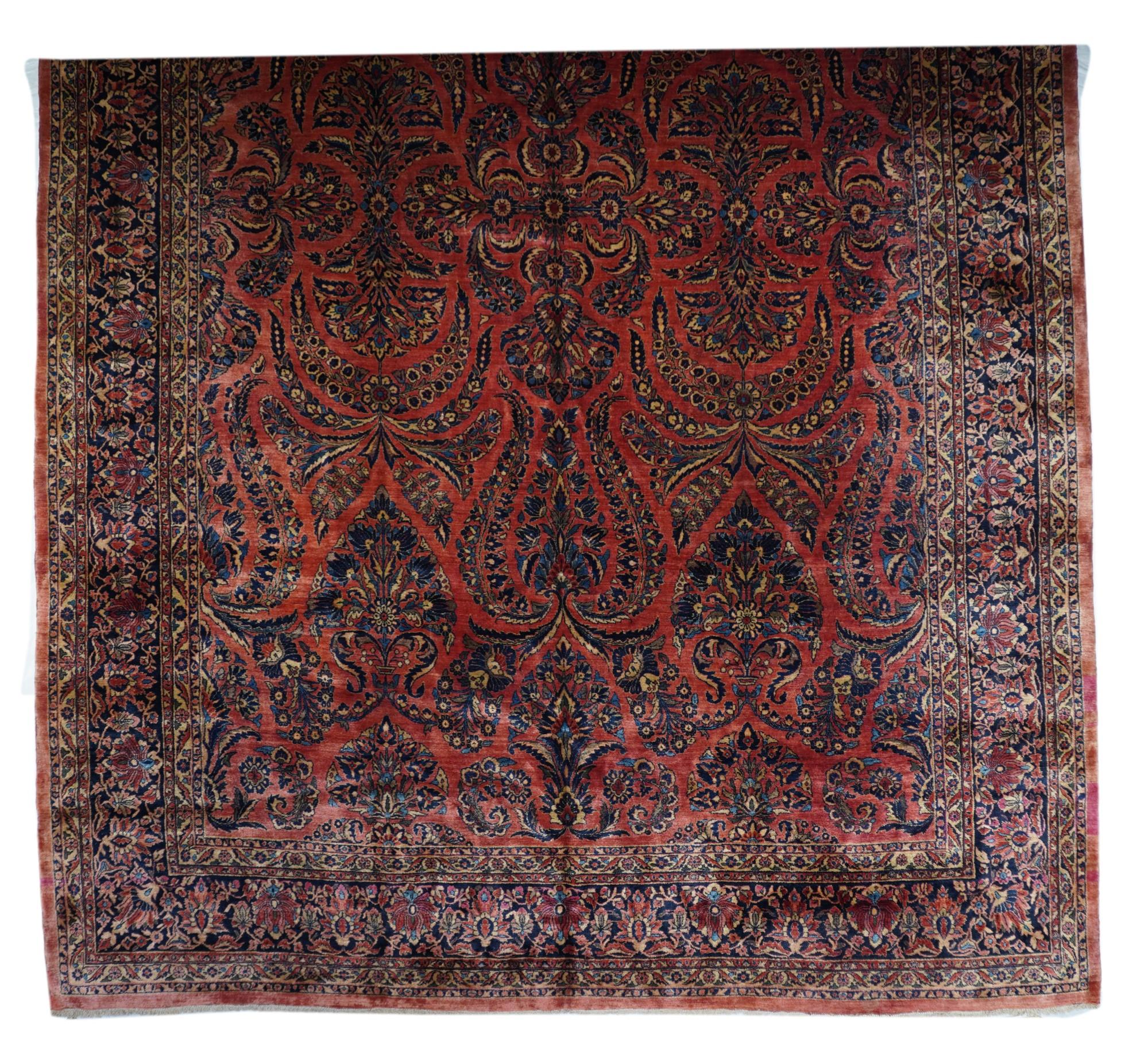 The scarlet – rose field of this exuberant “American style” west Persian village carpet shows vigourous floral sprays, flower clusters and barbed leaves, all set around a centre of 12 bitonal lancet leaves. Navy border with two varieties of in and