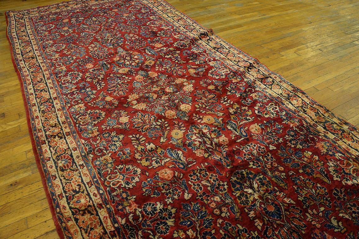 This unusually formatted Sarouk carpet has the classic mulberry red field well covered with characteristic interwar floral sprays grouped around a small central quatrefoil based medallion centre. The borders of this circa 1930 interwar long carpet