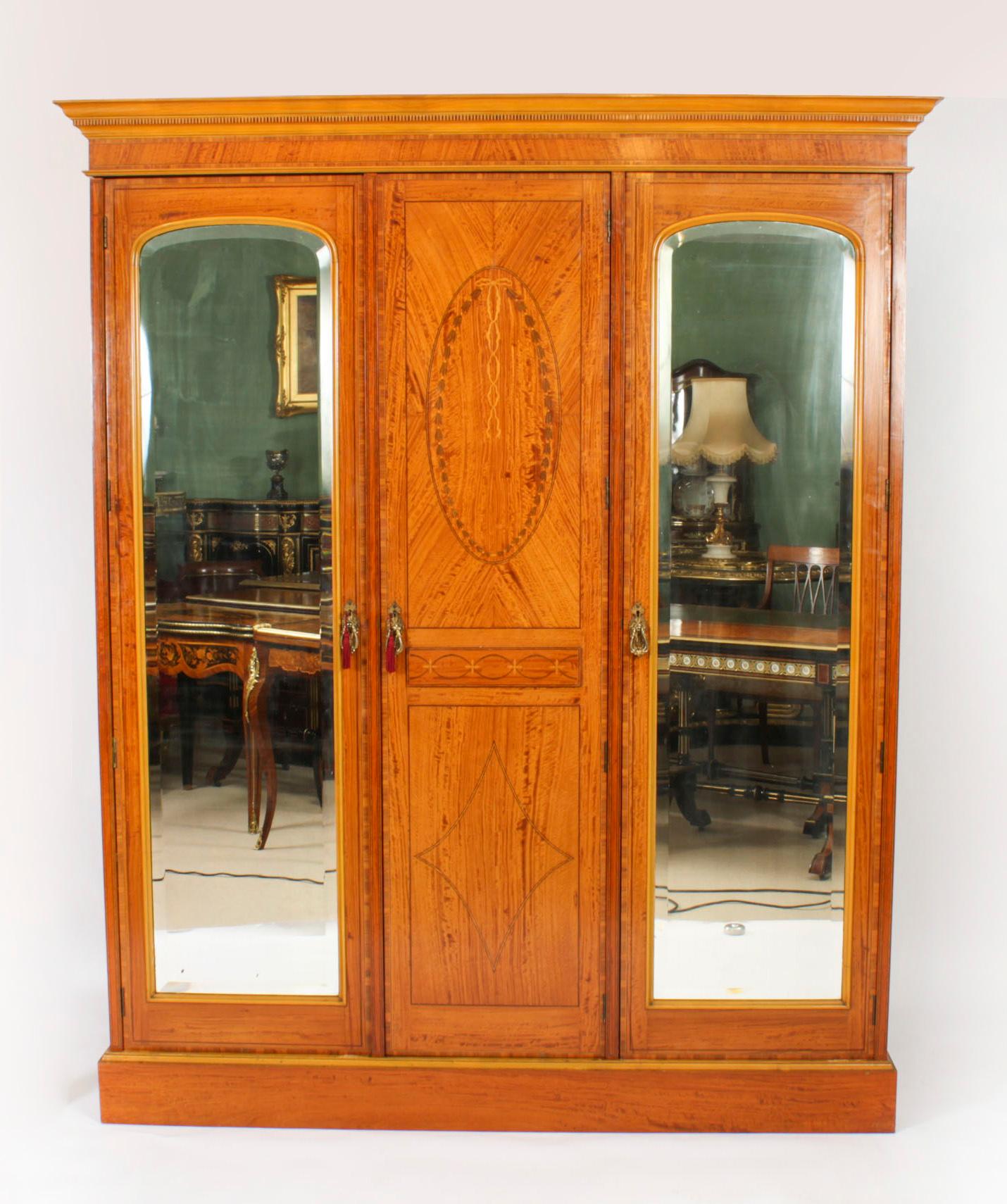 This is a large rare and impressive antique English satinwood, tulip wood banded and marquetry inlaid compactum wardrobe, by the world renowned cabinet maker and retailer Maple &Co, circa 1880 in date.
 
The central section has a panelled cupboard