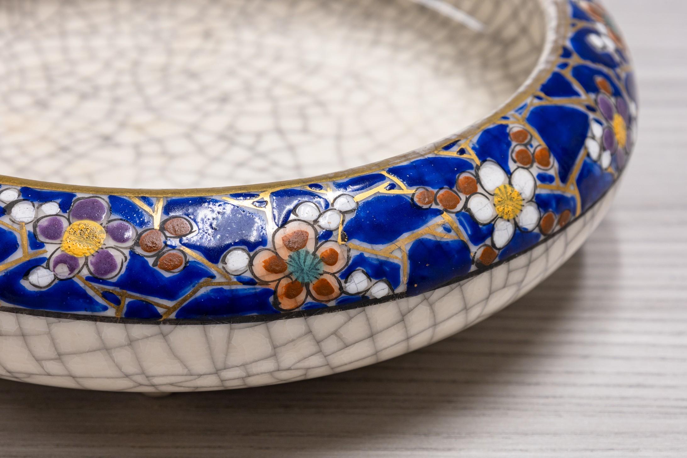 Diese antike Satsuma-Schale zeichnet sich durch ihre reiche kobaltblaue Glasur aus, die mit verschlungenen goldenen und mehrfarbigen Blumenmotiven verziert ist. Das Innere der Schale ist mit einer zarten Craquelé-Glasur versehen, die die