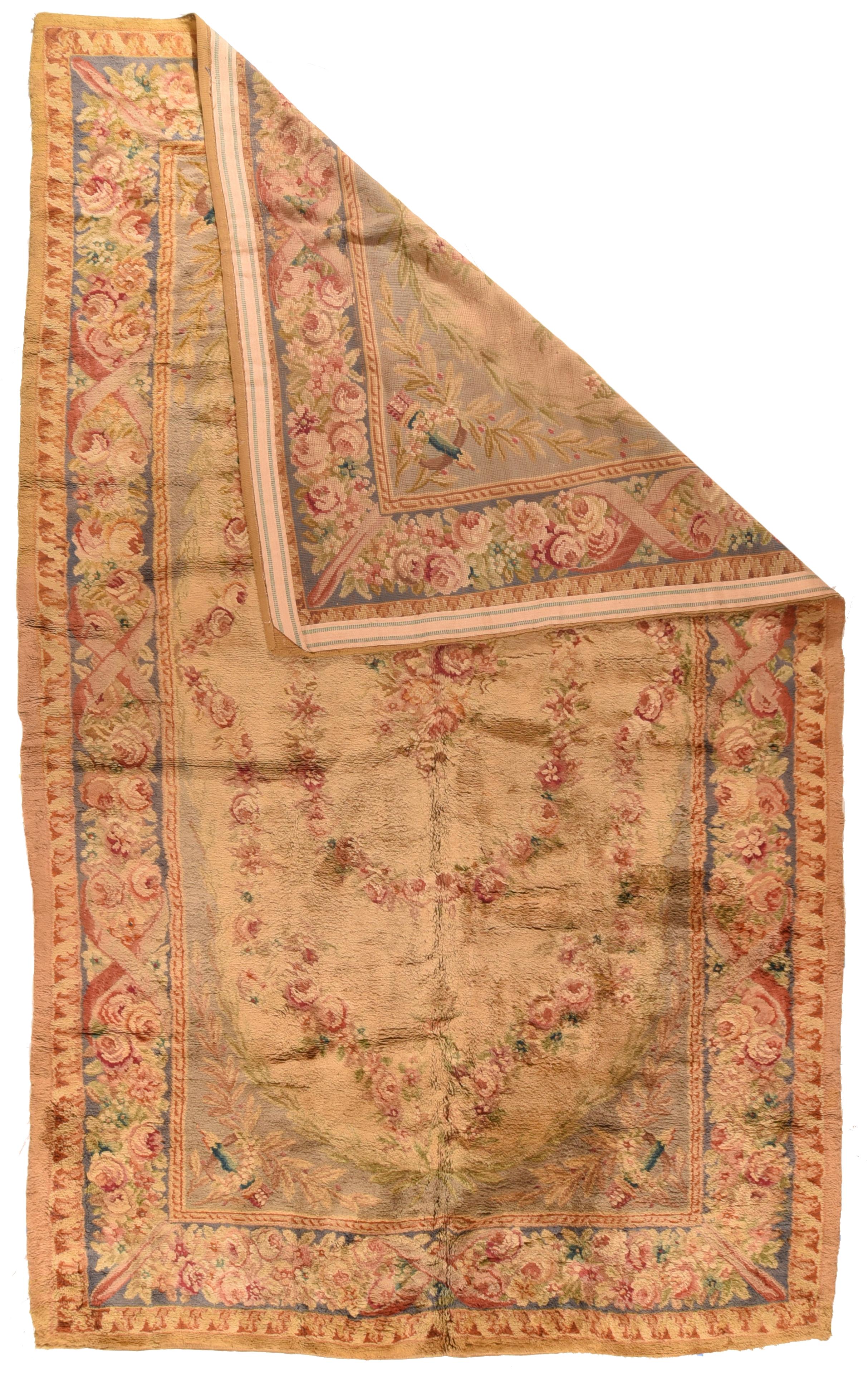 Antique French Savonnerie Rug 9'9'' x 16'0''. The straw cartouche-oval sub-field shows conforming and elliptical floral rose-accented wreaths surrounding a central rose bouquet. The supporting pale blue-grey ground shows in the laurel branch
