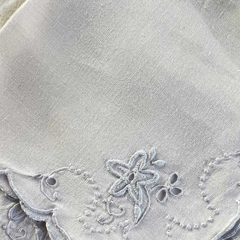 A set of three antique cloth napkins with scalloped edges and blue floral details. 