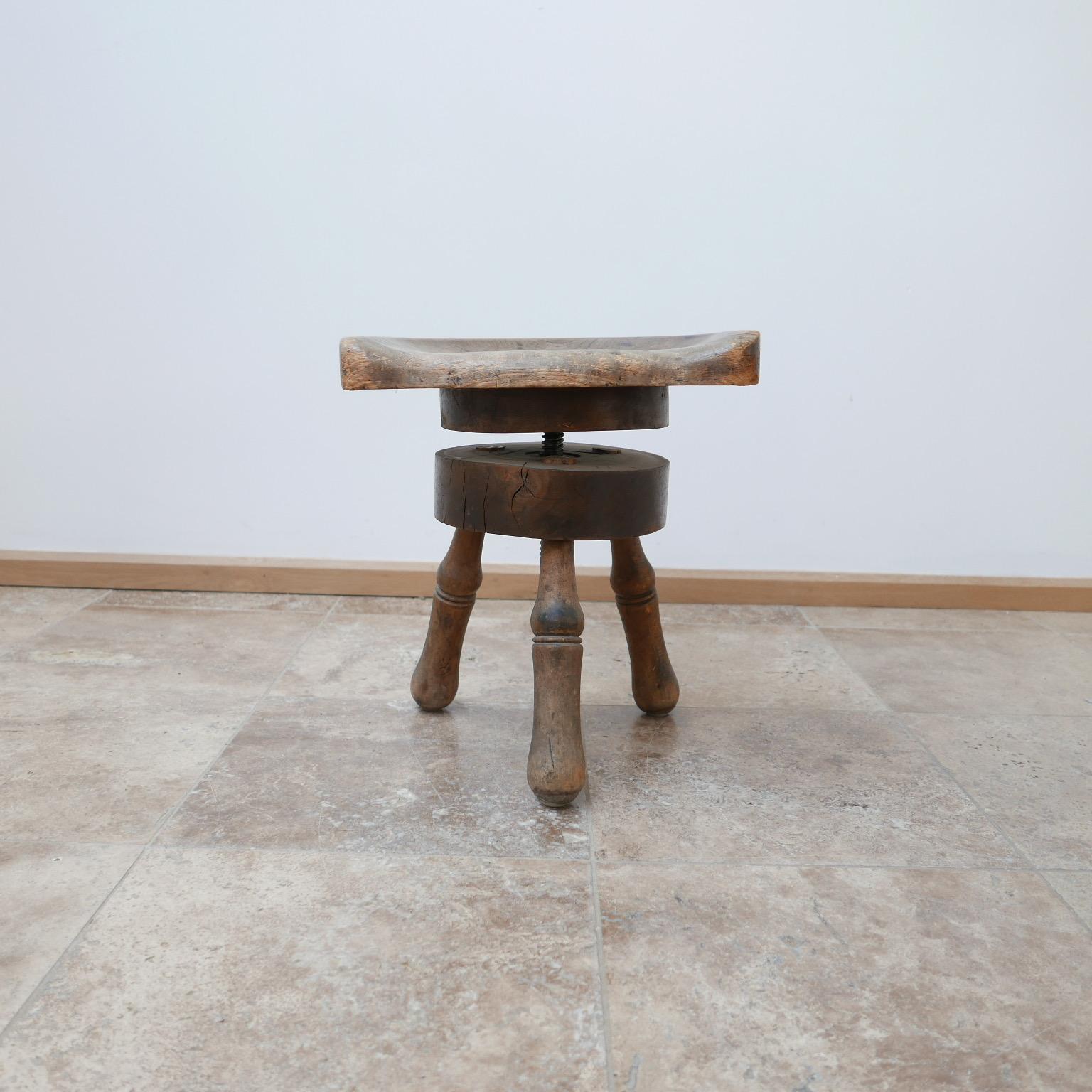 An early 20th century stool, adjustable in height.

A carved seat raised over three legs.

Adjustable by a turned metal pole rises and lowers the seat.

Raises from 42 H to 48 H in cm but can get slightly wobbly at the zenith.

Dimensions: