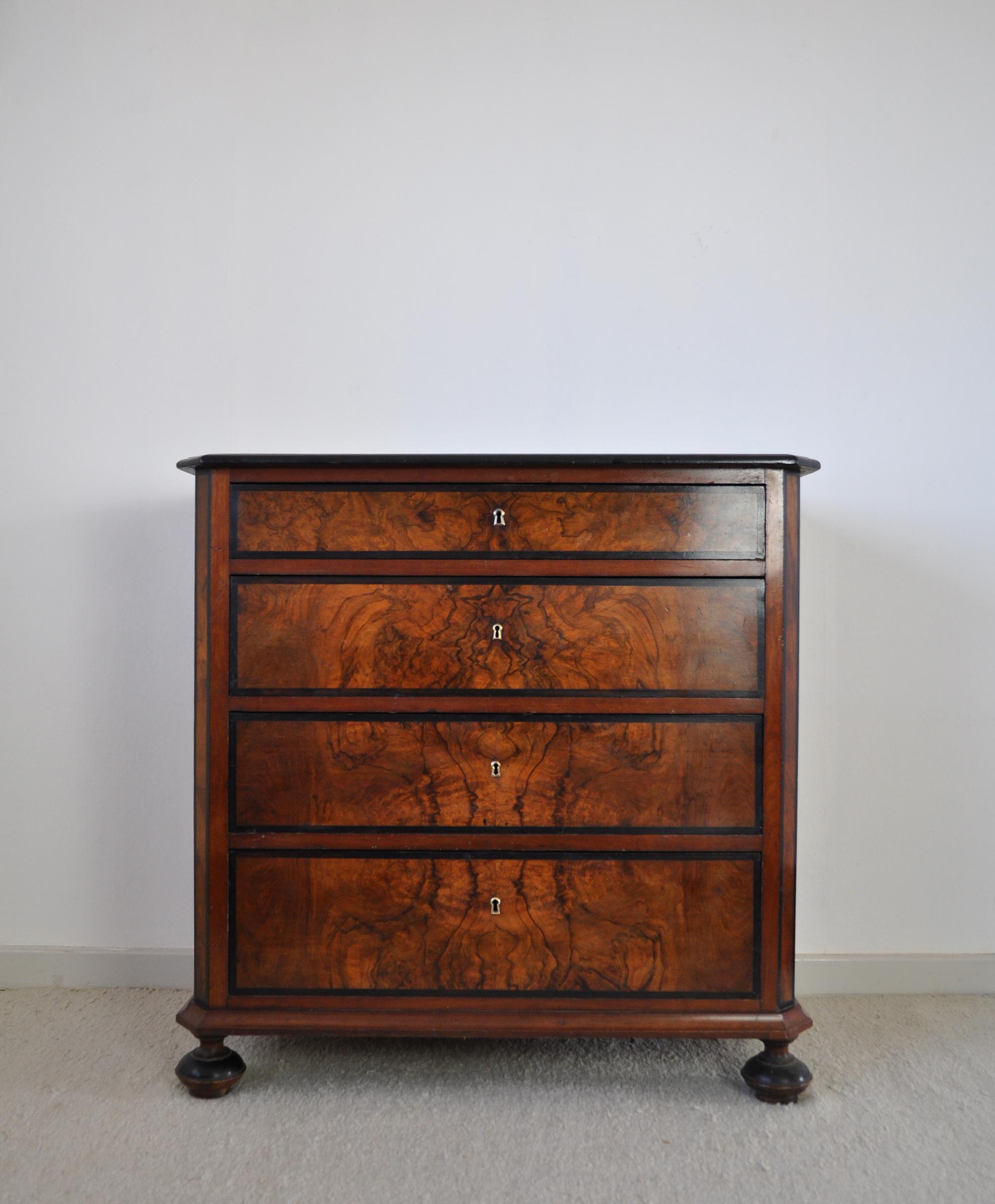 A fine chest of drawers or commode of flame walnut and mahogany with ebonized details throughout. The chest rests on original turned front feet and square back feet and features four storage drawers, offering a shallower one at the top. 19th