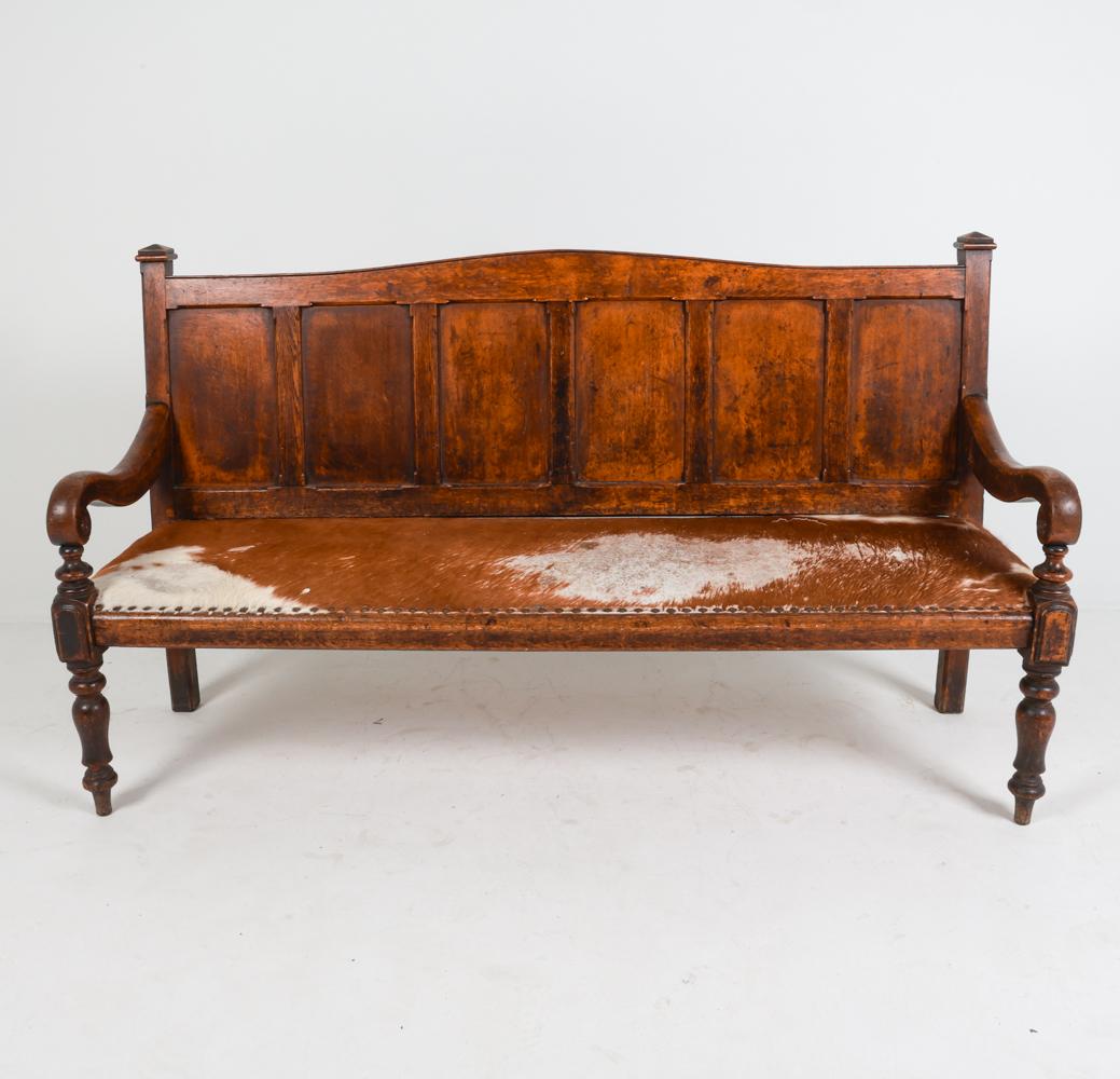 This settle sofa brings one into an earlier and more rustic period of time. Crafted from solid hand-carved oak wood, this sofa is handsome and sturdy, despite its age. The oak is darkened in tone, further indicating its age and use over the