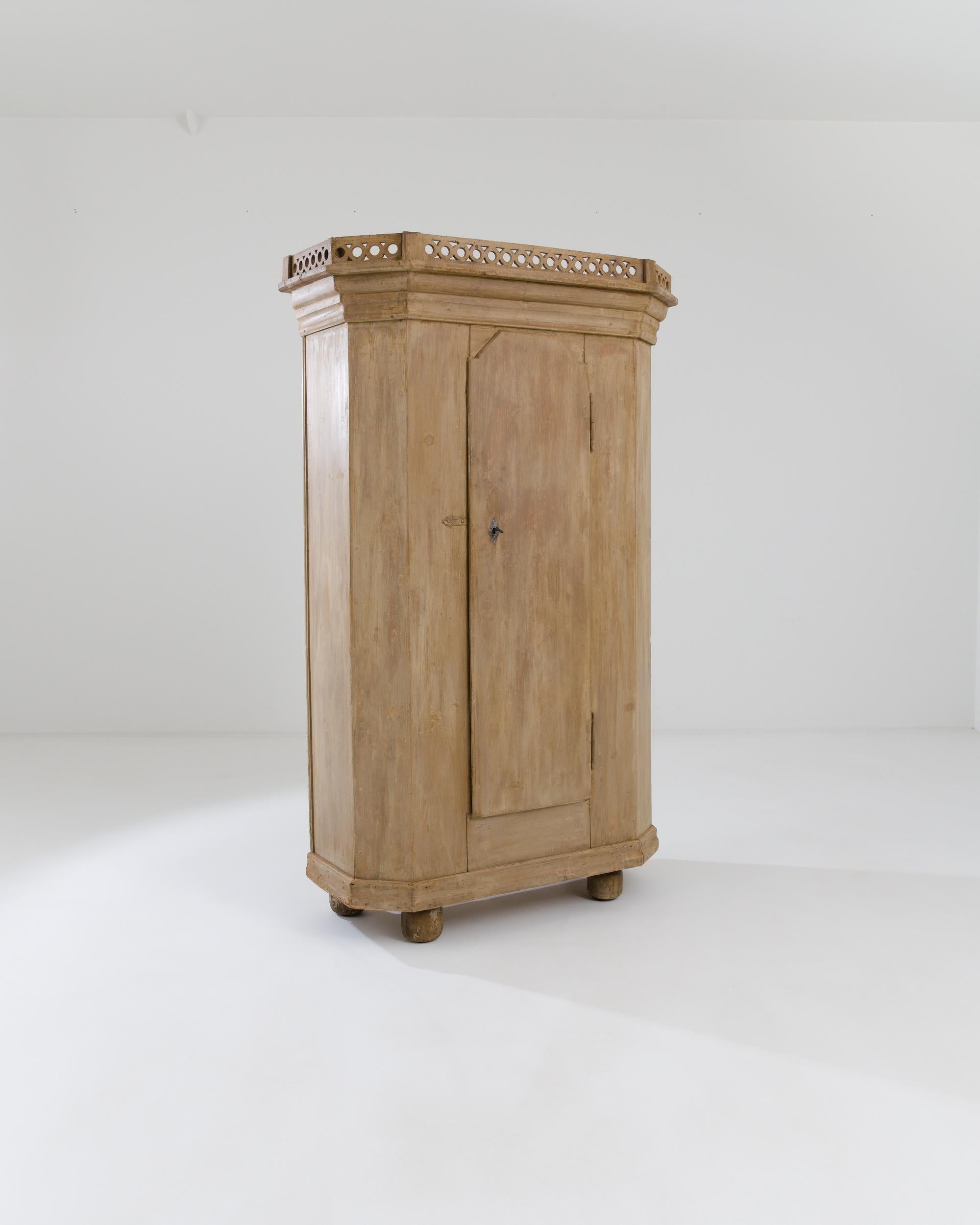 A wooden cabinet made in 20th century Scandinavia. With a sturdy, wide stance, rounded feet, and top resembling a castle wall, this curious cabinet emits a powerful yet homely and approachable aura. Its fortress-like door swings outward to reveal a