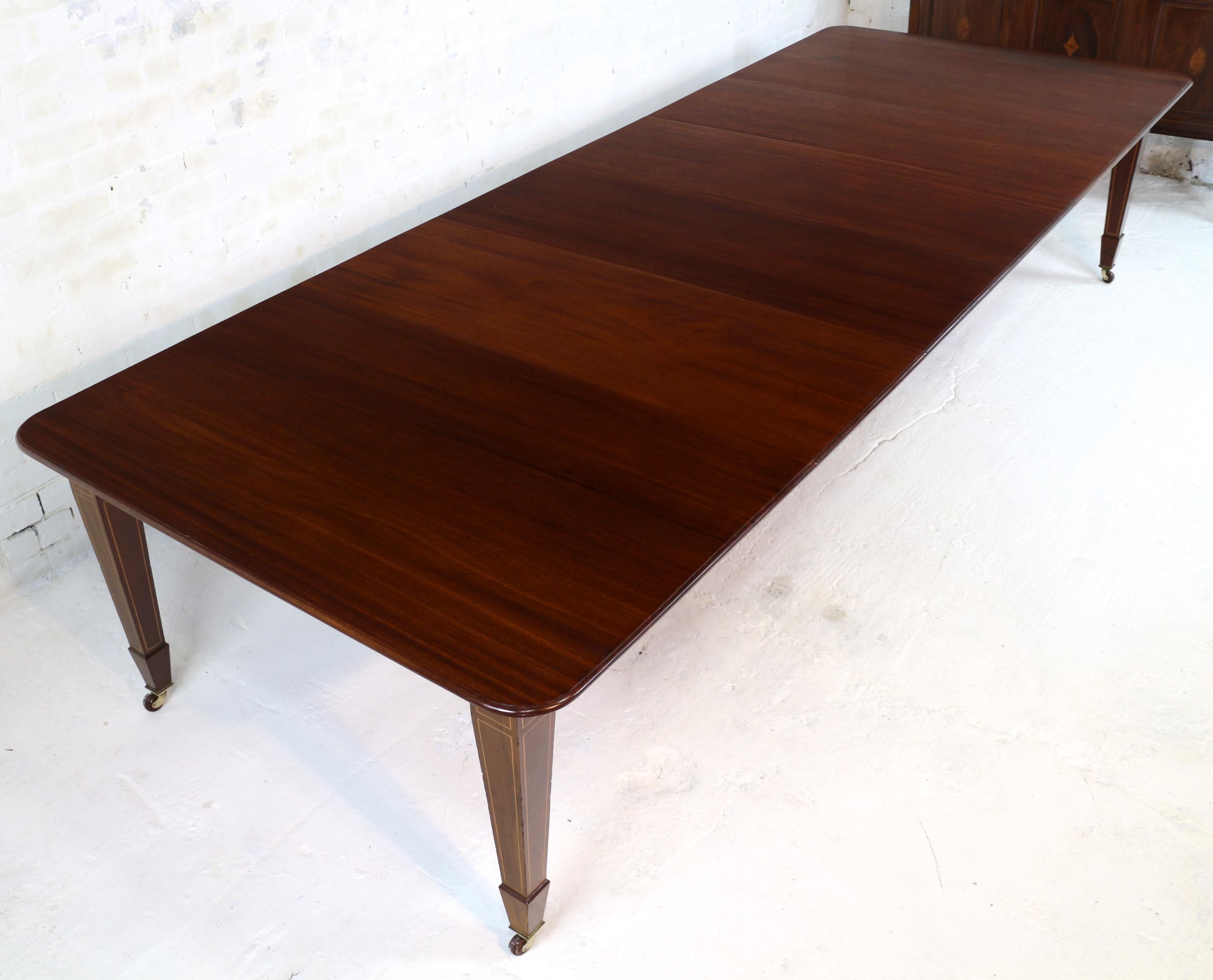 A super late Victorian/Edwardian Scottish 12ft wind-out mahogany and inlaid Sheraton style extending dining table and leaf holder by James Garvie & Sons of Aberdeen. The dining table with rounded rectangular top with a moulded edge and standing on