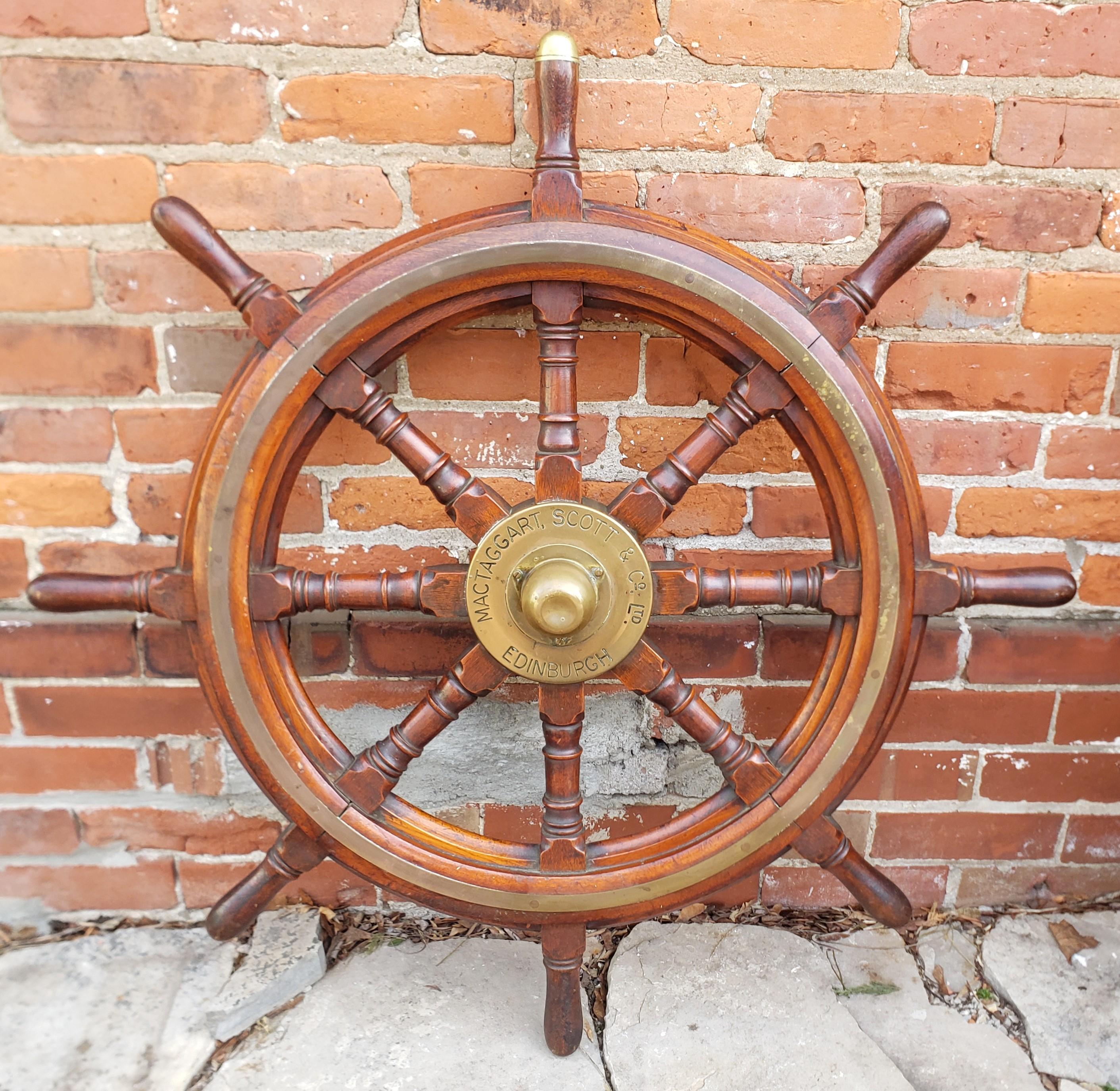 This antique ship's wheel was made by the MacTaggart, Scott & Co. of Edenborough, Scotland and dates to approximately 1900 and done in the period style. This ship's wheel is composed of solid oak with a brass hub fitting with the maker's mark on the