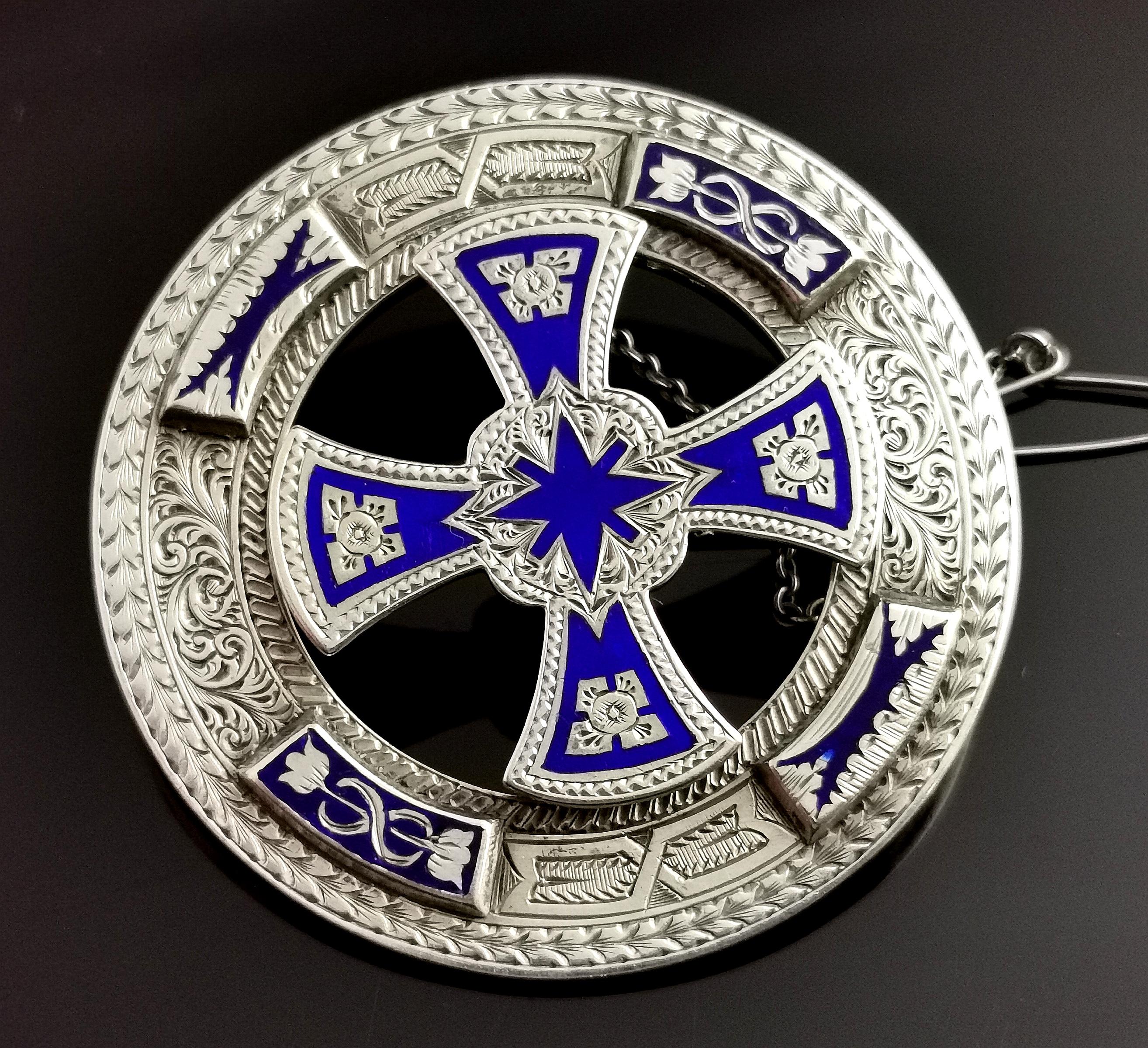 A beautiful and highly detailed antique Scottish sterling silver and cobalt blue enamel brooch or kilt pin.

It is a large sized brooch, circular in shape with a mounted celtic Cross to the centre.

It is heavily engraved all over and has four