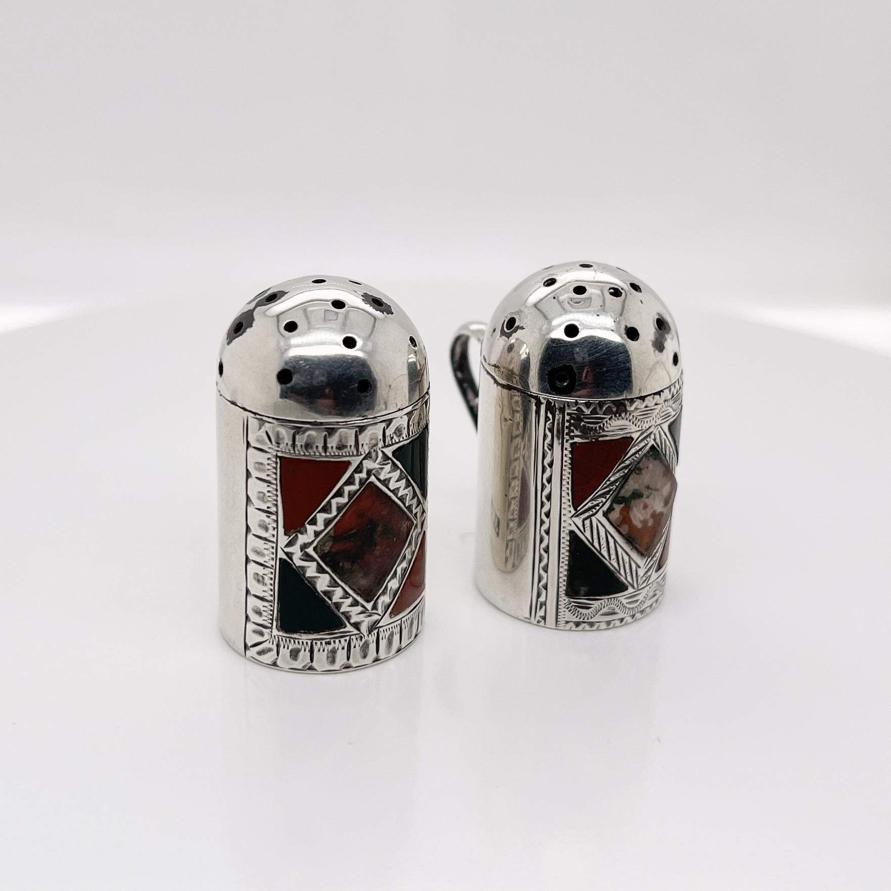 A fine pair of antique Scottish pepperettes.

By J. W. Kirwan & Co. of Edinburgh, Scotland.

In the form of miniature tankards. Center-set with diamond shaped agate stones that are flanked by red & green enamel triangles and bright cut