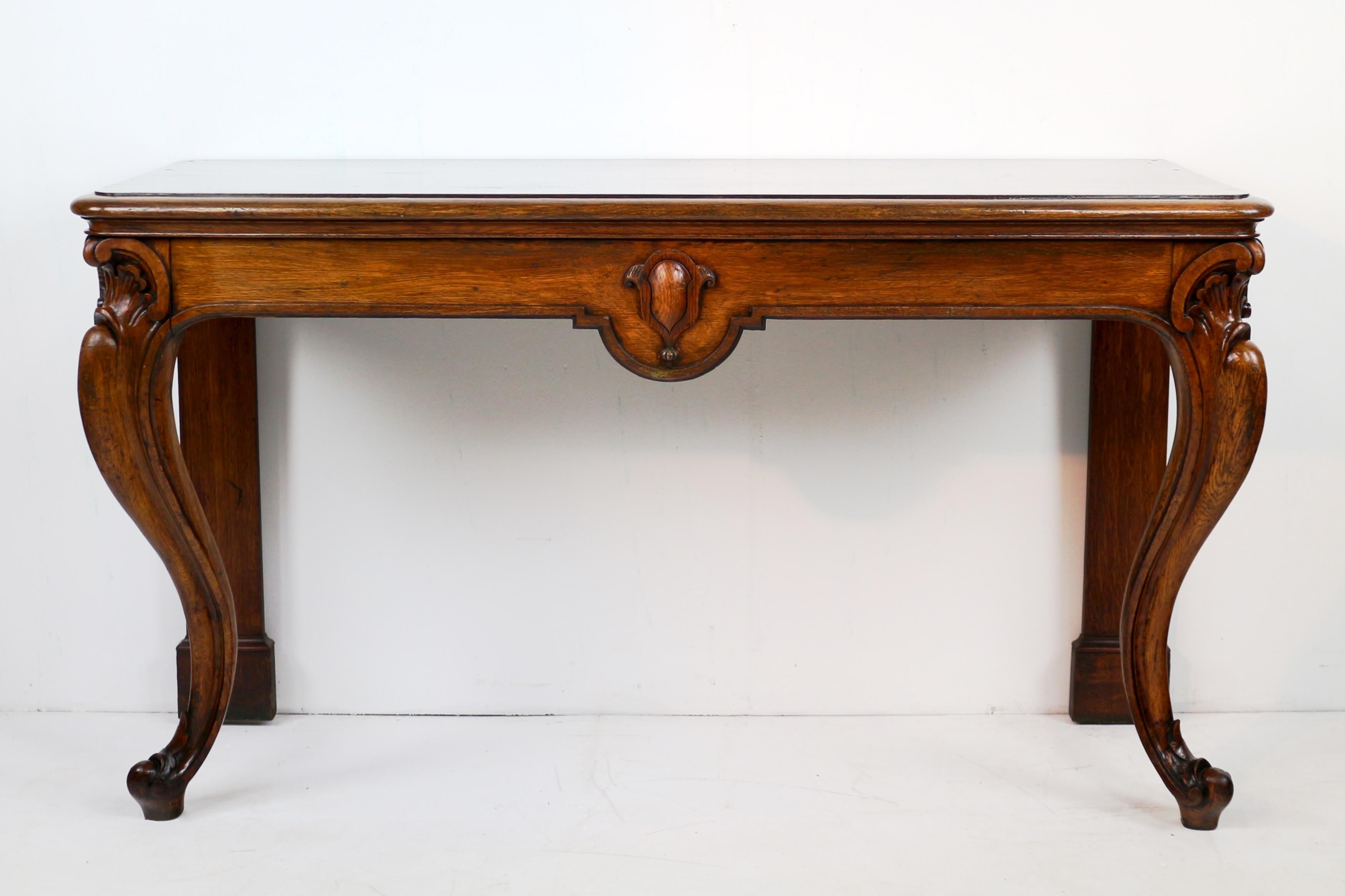 A large Scottish William IV oak hall or serving table dating to the early 19th century, circa 1830.  With a moulded rectangular top above a shaped frieze with central shield cartouche and raised on well carved cabriole legs to the front with leaf