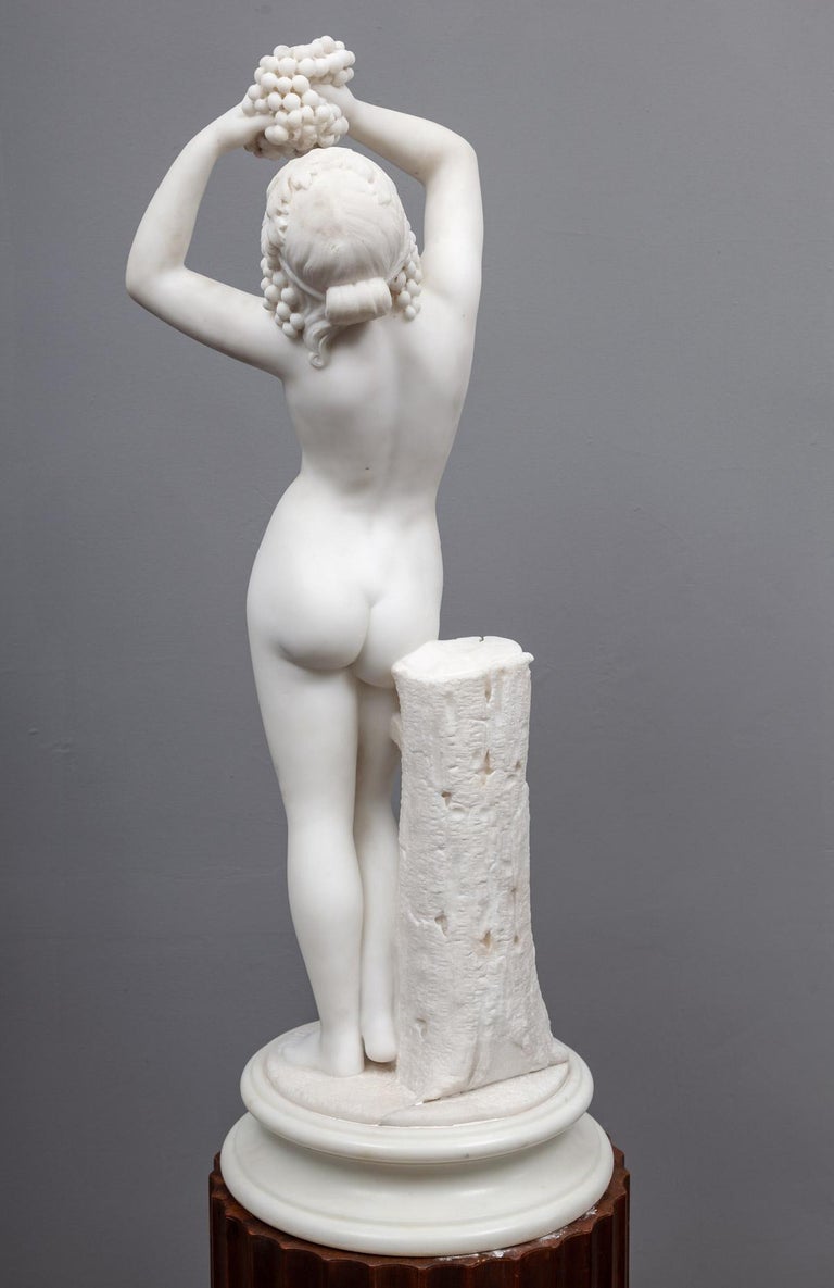 A beautifully carved antique statuary Carrara marble sculpture of Aphrodite. Depicted in the nude, holding a bunch of grapes and standing beside a tree stump.

Aphrodite is an ancient Greek goddess associated with love, beauty, pleasure, passion
