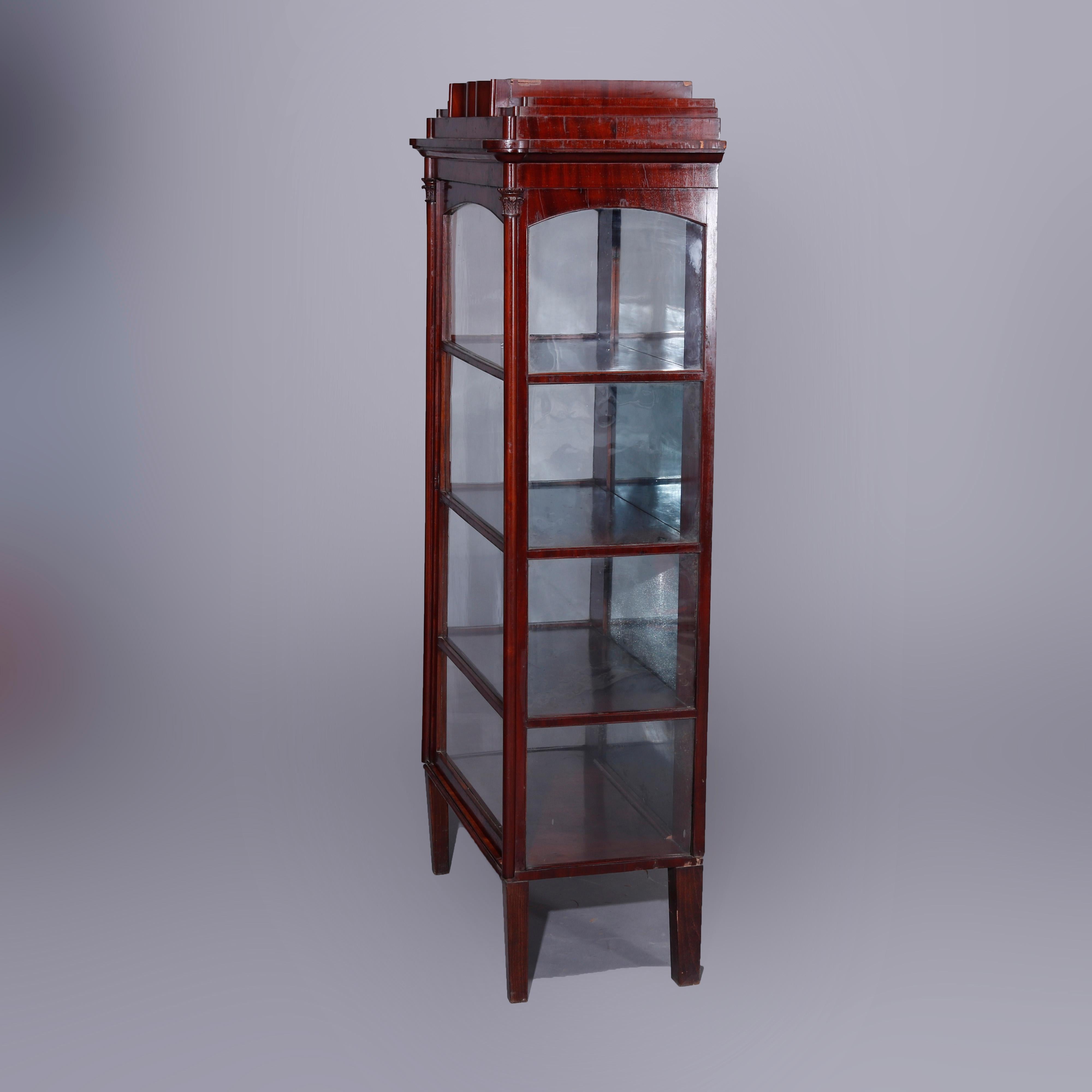 An antique Second American Empire neoclassical vitrine or china cabinet offer flame mahogany construction with stepped crest surmounting case with single glass door opening to a mirrored and shelved interior and flanked by Corinthian column