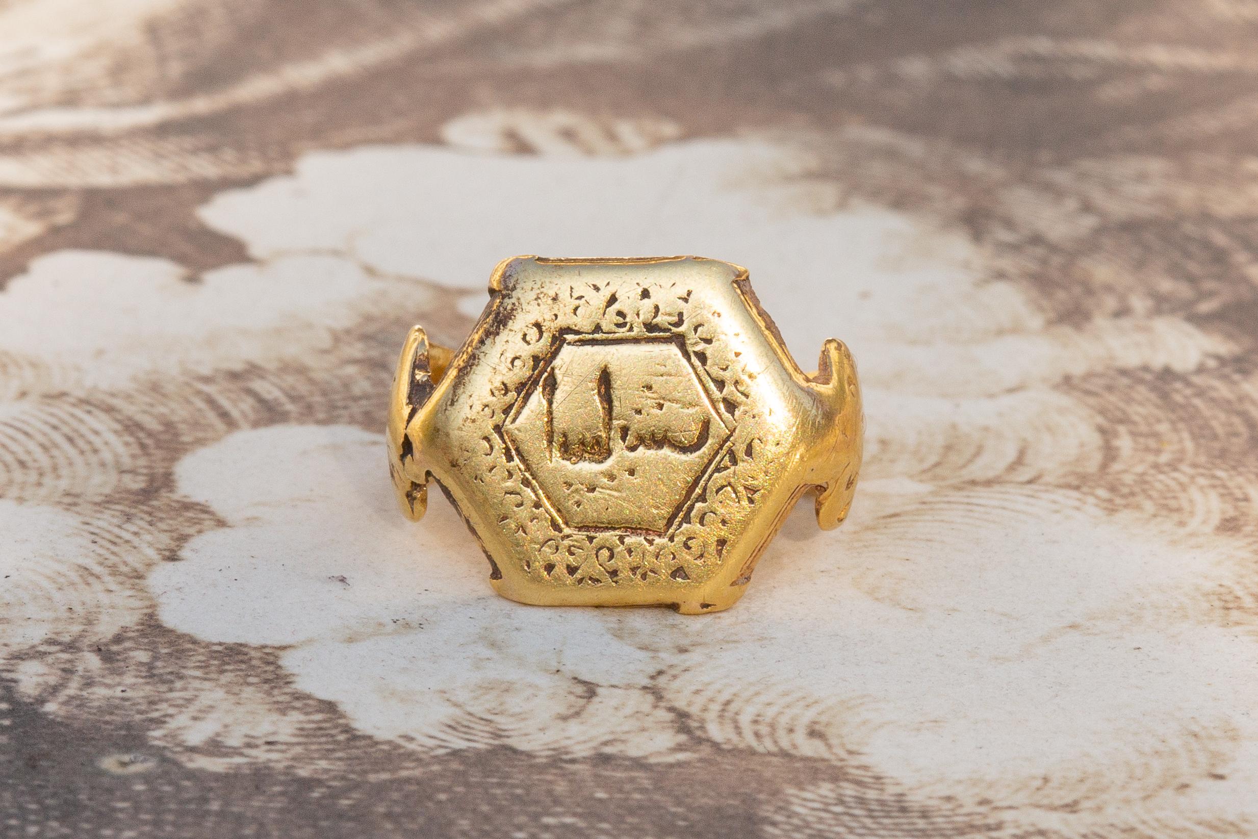 This quite small (yet mighty) 21K gold ring dates to the 11-13th century Seljuk dynasty. The hexagonal bezel features a negative cursive inscription within a border containing arabesque scrolled patterns. There is a waisted section between the bezel