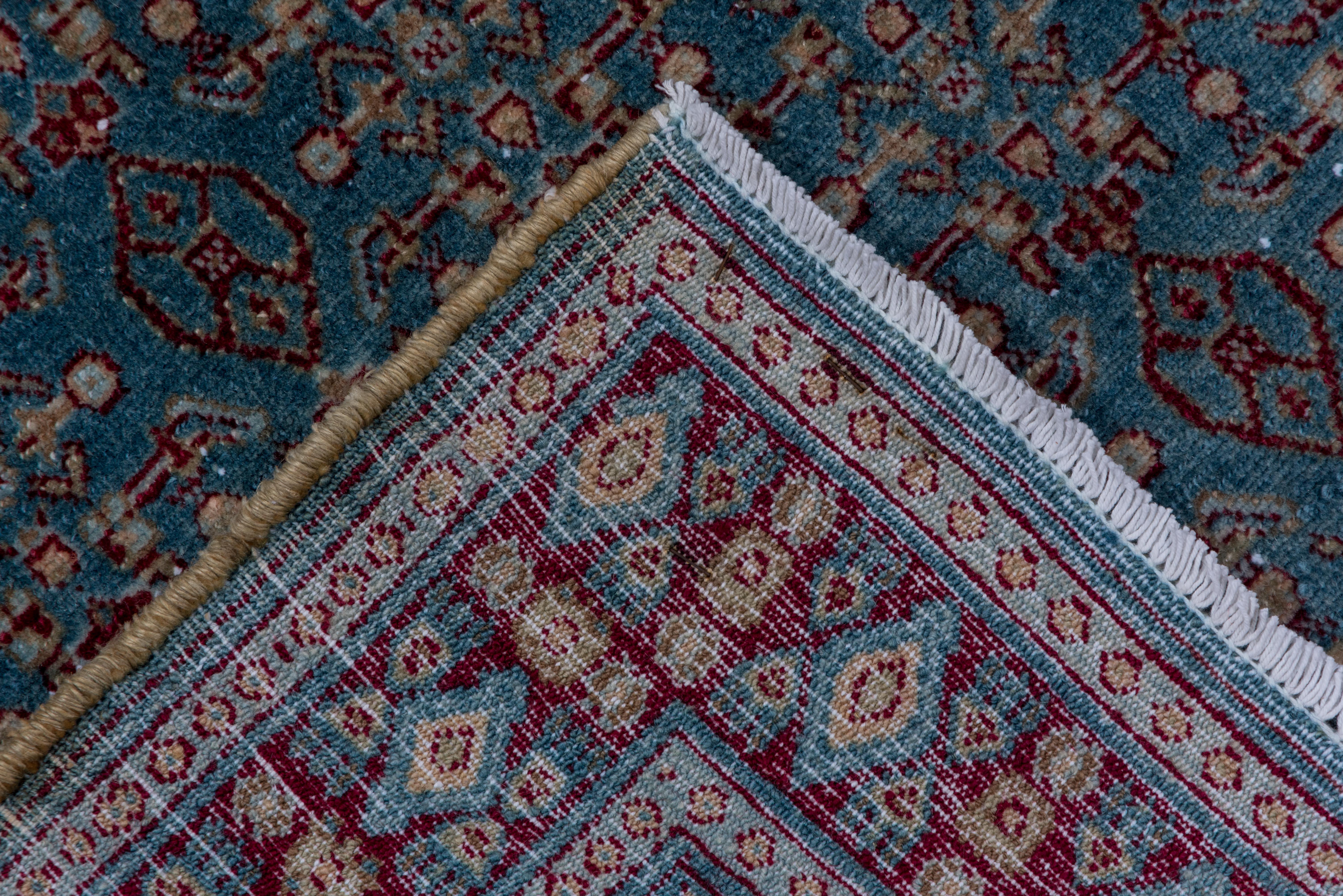 This antique Senneh rug features a meticulously rendered Herati design in a tight allover pattern across a cool blue field. Burgundy, ivory, and soft blush tones form a rhythmic lattice of rosettes, palmettes, and diamond motifs, framed by a classic
