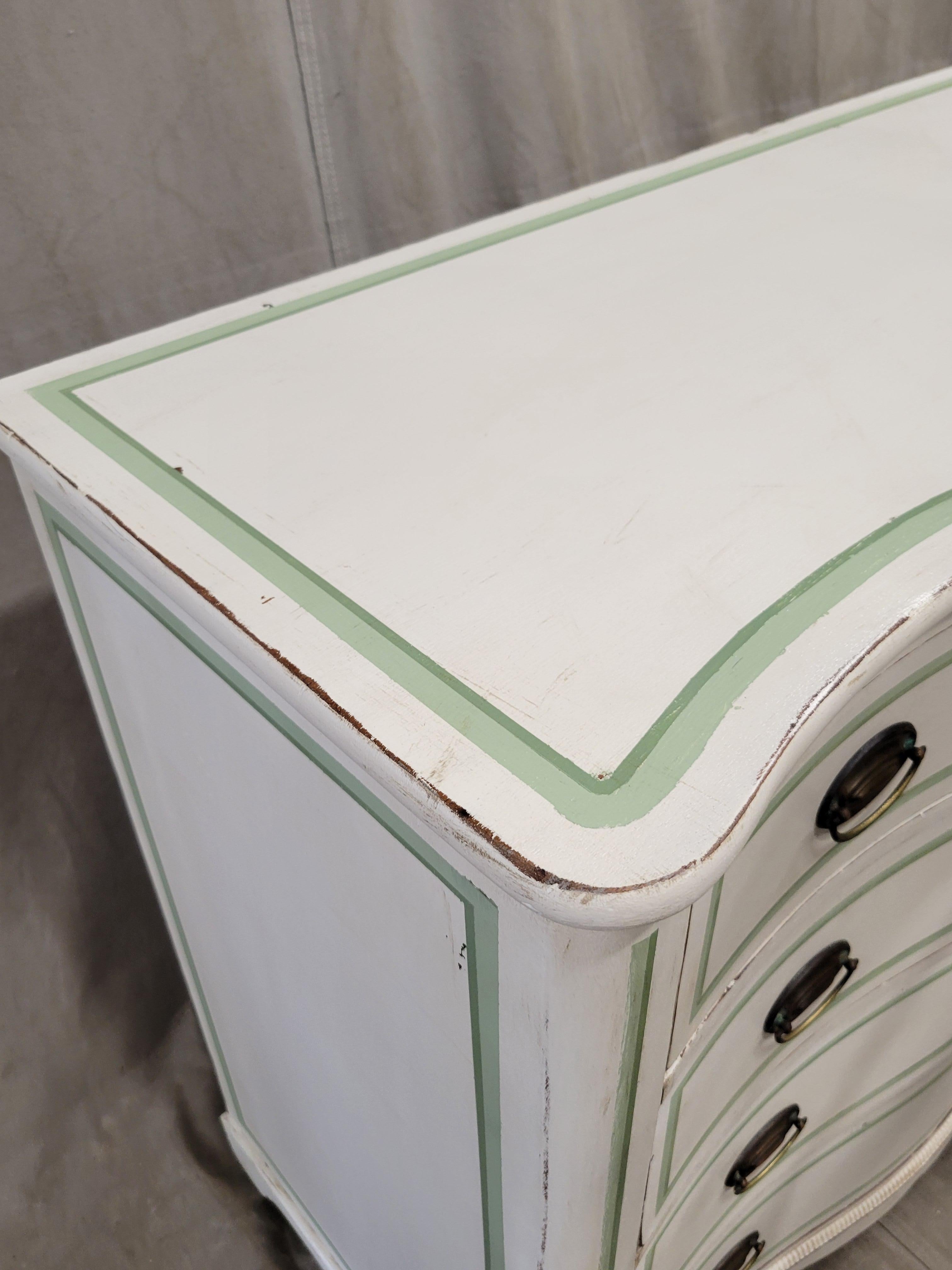 An absolutely charming antique hand painted serpentine front walnut dresser with distressed white paint and green French line motif. The four drawers glide smoothly and offer plenty of storage. Brass tone handles are original to the dresser.