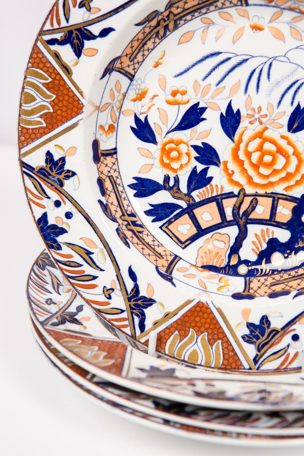 This set of a dozen 19th century English Imari soup or pasta dishes is painted in iron red, deep blue, and gold.  Each dish is fully decorated showing a traditional garden scene including a large orange peony, the branches of a willow tree, blue