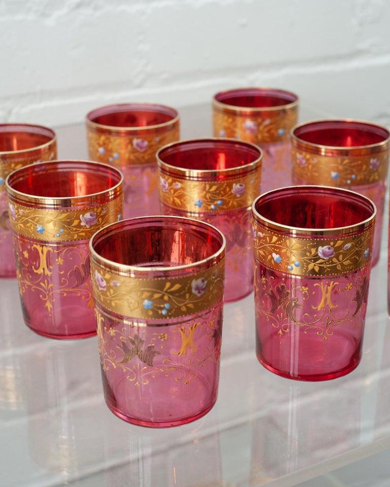 Un ensemble habituel et délicat de 9 verres à pied antiques de Moser, à la canneberge et à l'or doré. Ce verre fin de couleur canneberge est doré à l'or fin avec des motifs de volutes d'or et peint à la main avec des fleurs.
 
