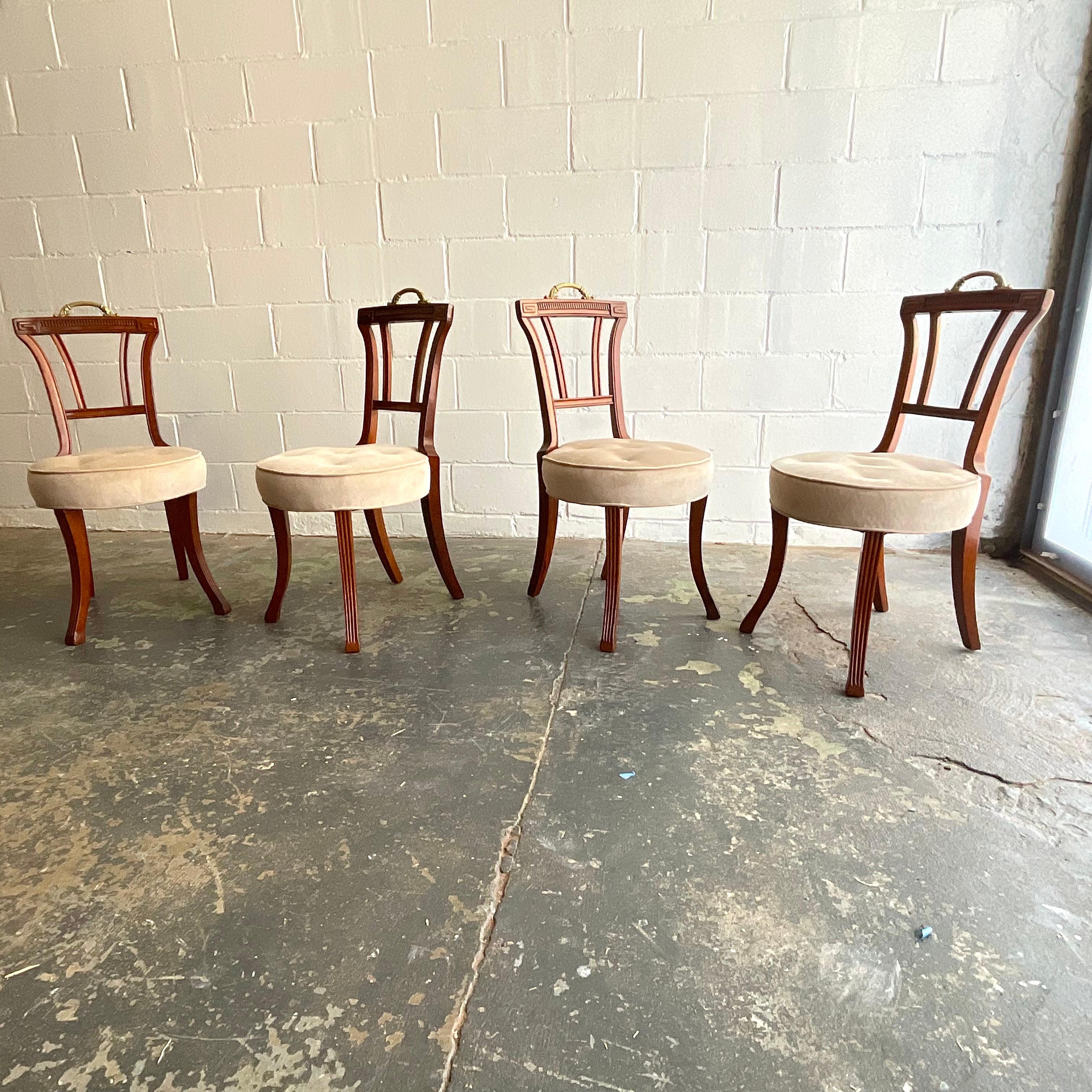 Petite yet comfortable set of four dining or side chairs in wonderfully patinated mahogany with original brass handles. This design features fluted front saber legs with Greek classical motif carved crest rail, and traditional spring stuffed seats.