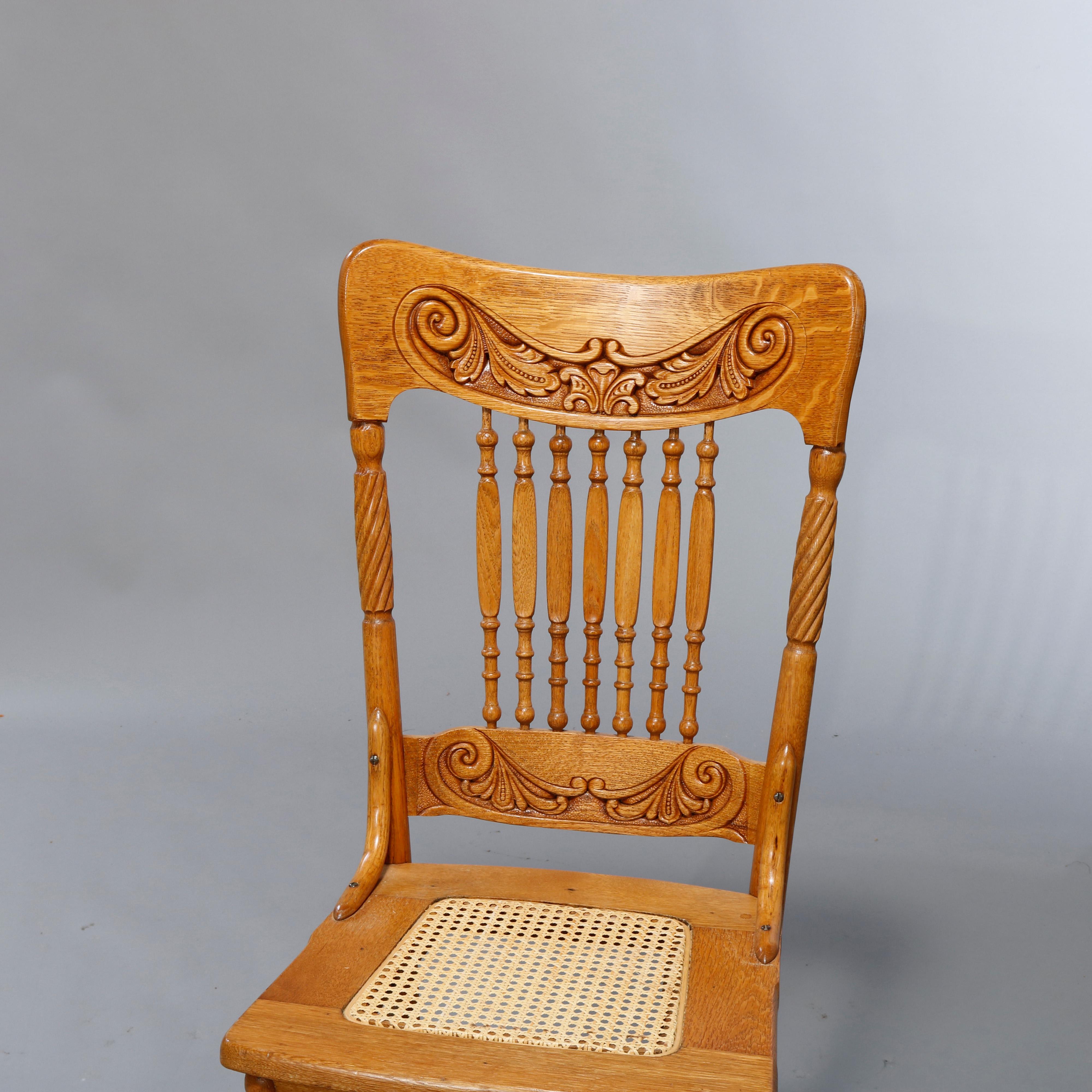 A set of twelve antique dining chairs offer oak construction with foliate pressed rails over spindle backs and caned seats raised on turned and tapered legs, c1910.

Measures: 40.5