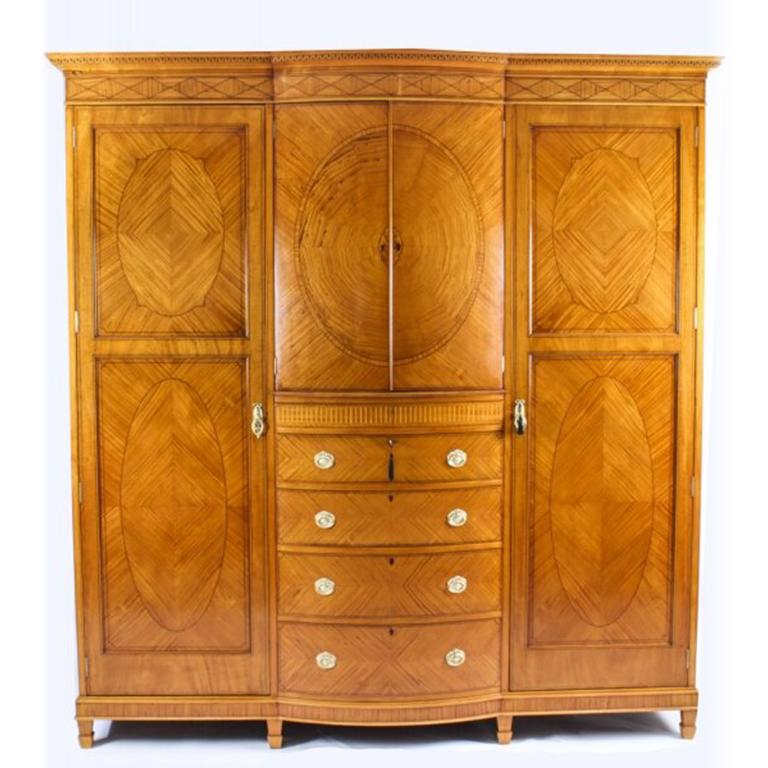 An antique English seven piece satinwood and ebony strung bedroom suite, circa 1880 in date.
 
Comprising a bowfront wardrobe with Greek key dentil cornice above two cupboard doors enclosing a shelf, four drawers below flanked by cupboard doors
