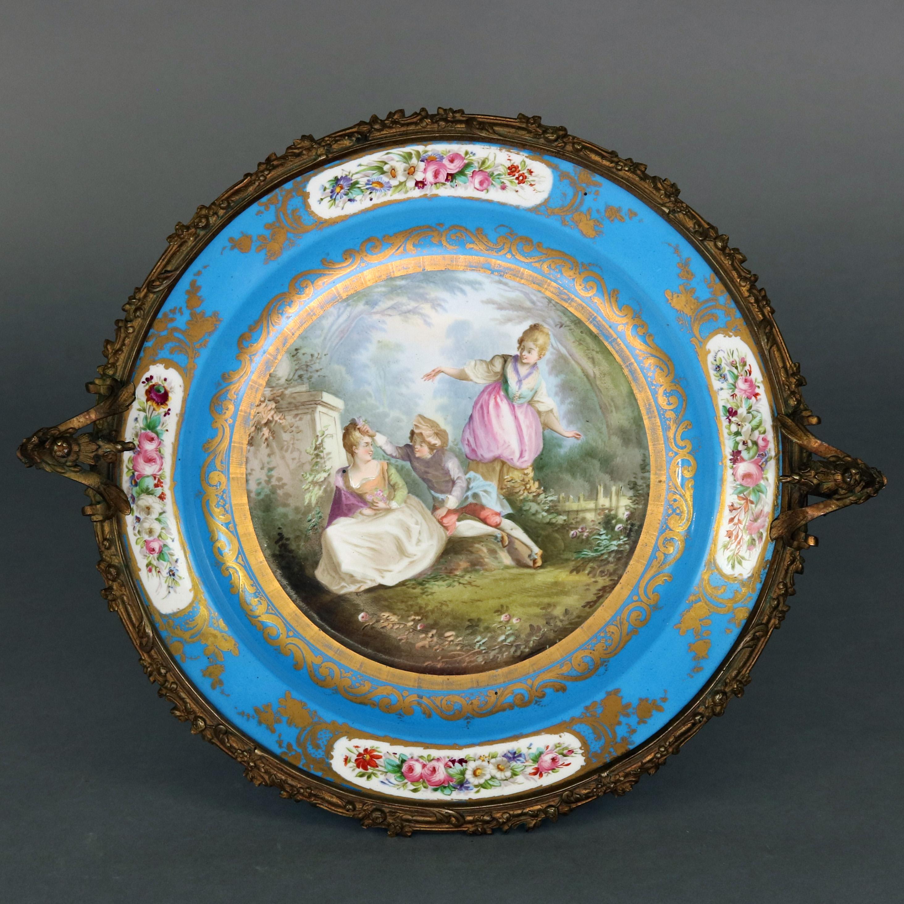 An antique Sevres School porcelain pictorial charger features hand painted central courting scene in countryside setting and having Sevres signature gilt decorated blue rim having floral reserves, seated in floral and foliate form double handle