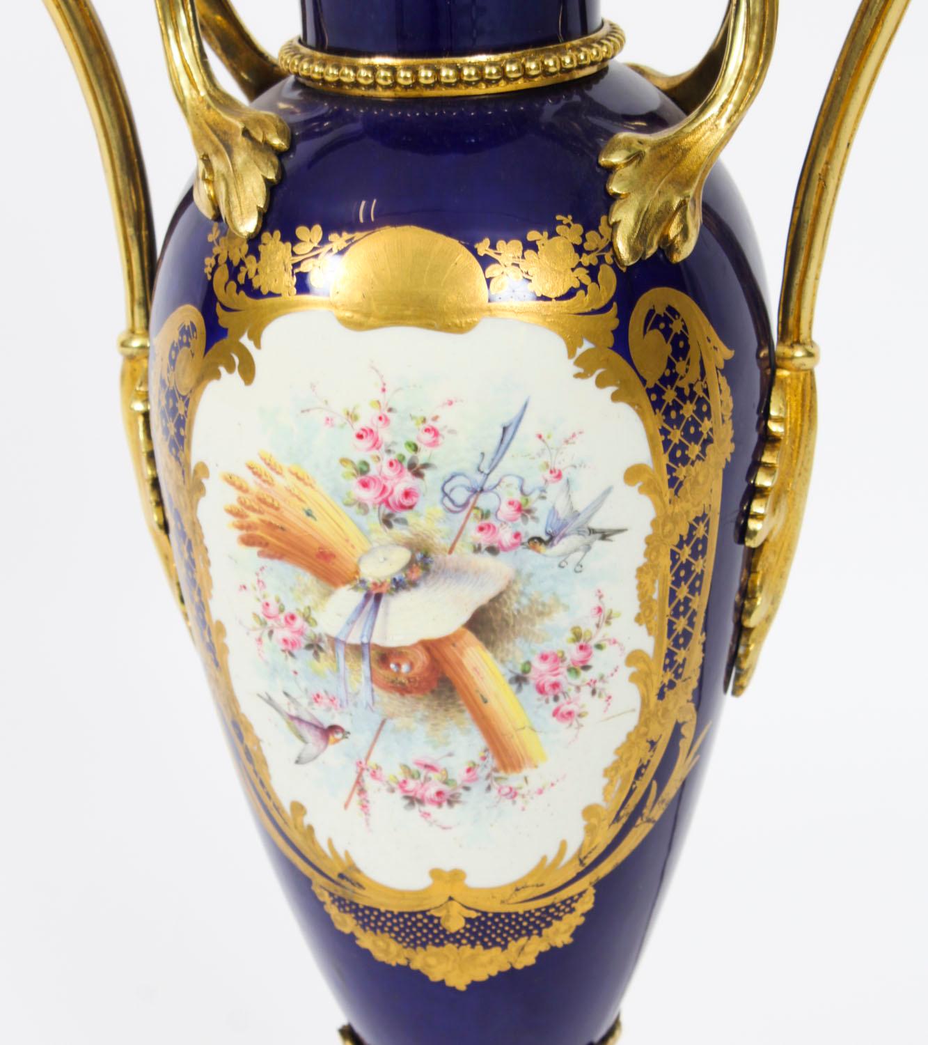 Il s'agit d'un superbe vase à deux anses de style Sèvres, peint à la main en porcelaine bleu cobalt et monté en bronze doré, datant d'environ 1880, transformé par la suite en lampe.

Le corps en porcelaine en forme de grand vase est peint de