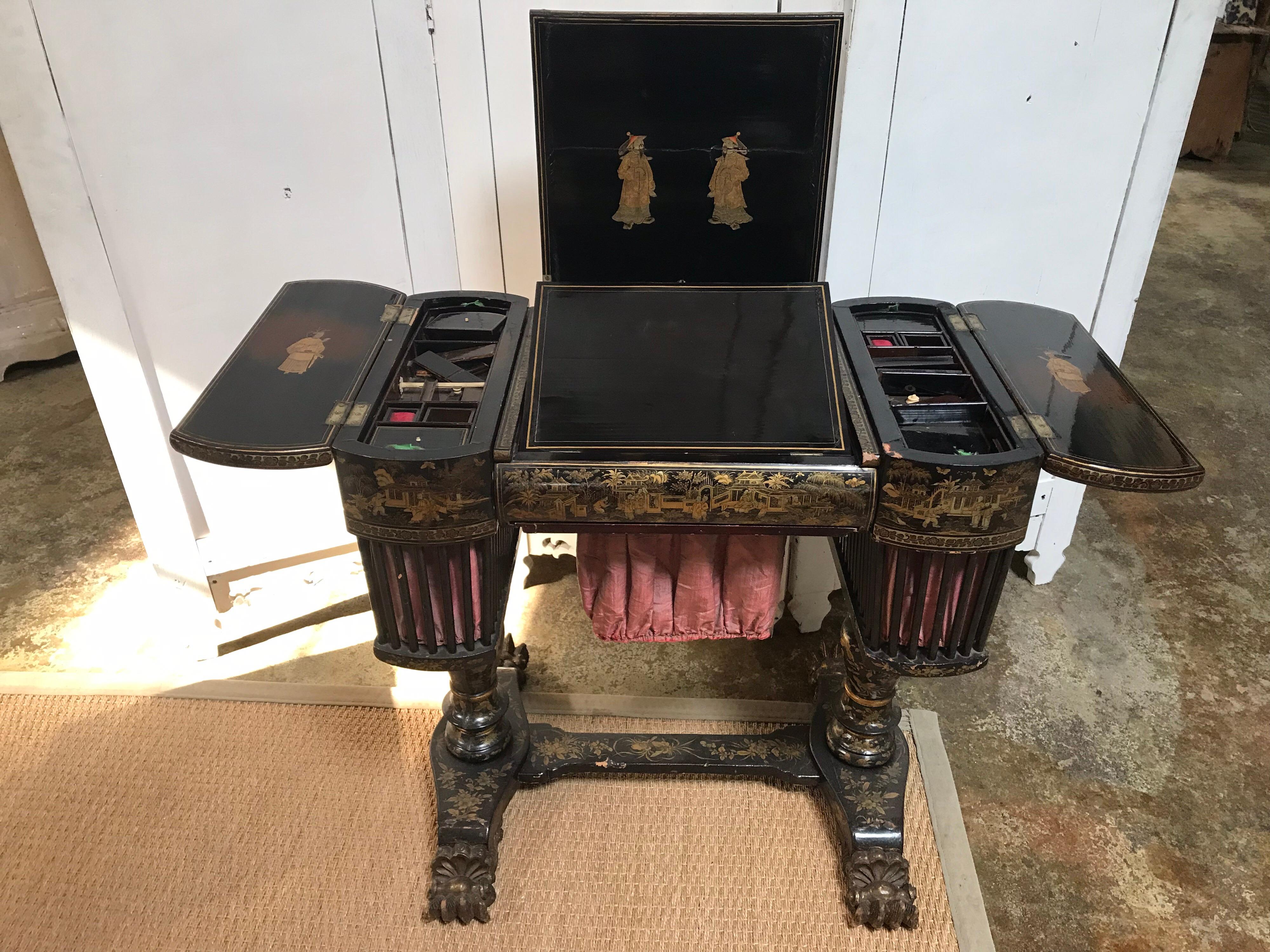 Cette table de couture ancienne est magnifiquement décorée, de la base au plateau, d'histoires et de motifs laqués de chinoiserie dorée. Cette table, qui date du début du XIXe siècle en Angleterre, comporte deux compartiments latéraux pour le