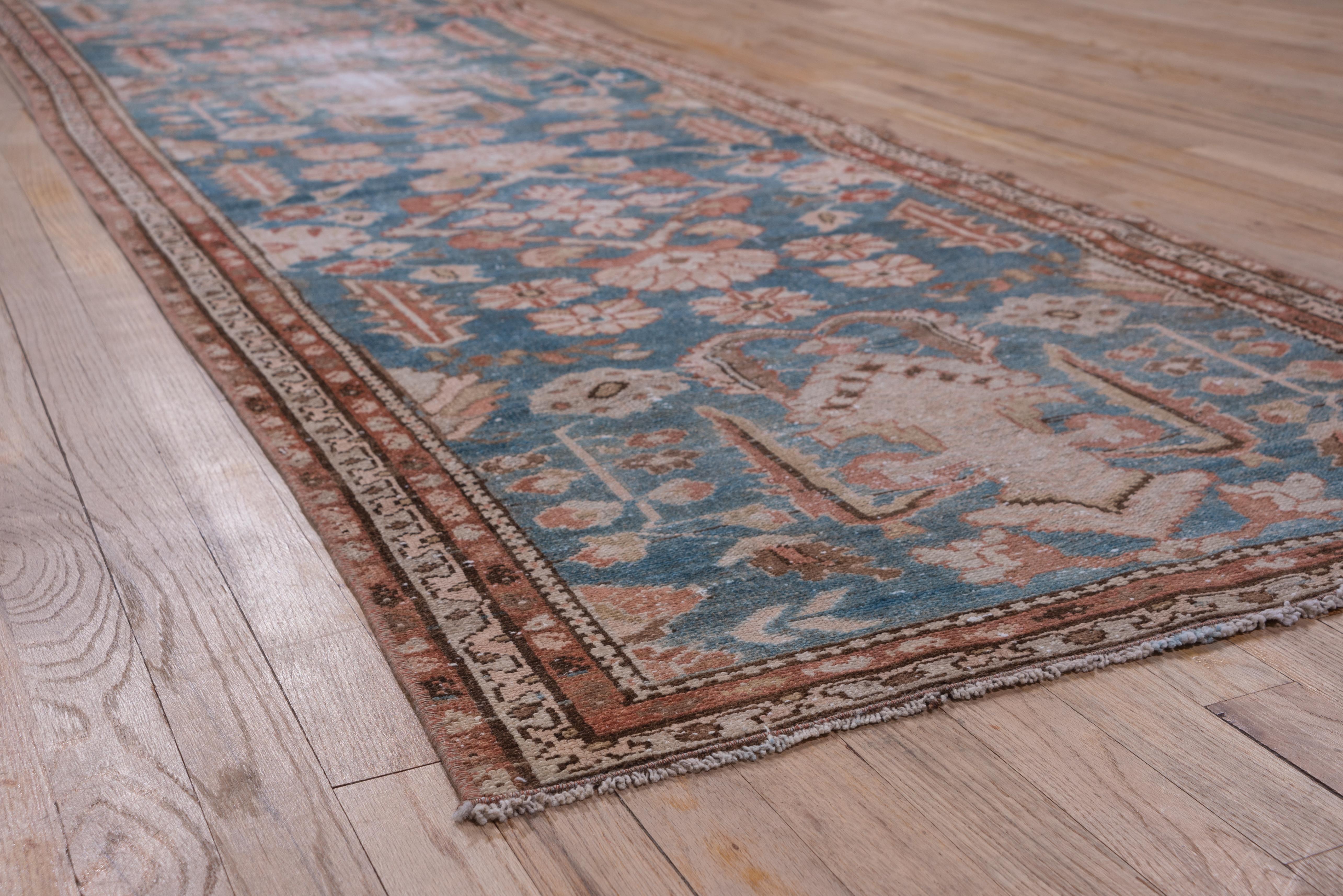 This west Persian runner shows ivory cruciforms embraced by ragged leaves, with a background scatter of tall flowers, serrated leaves, open lozenges and smaller rosettes on a light blue-grey field. The open lozenges are in the Herati style. Rust and
