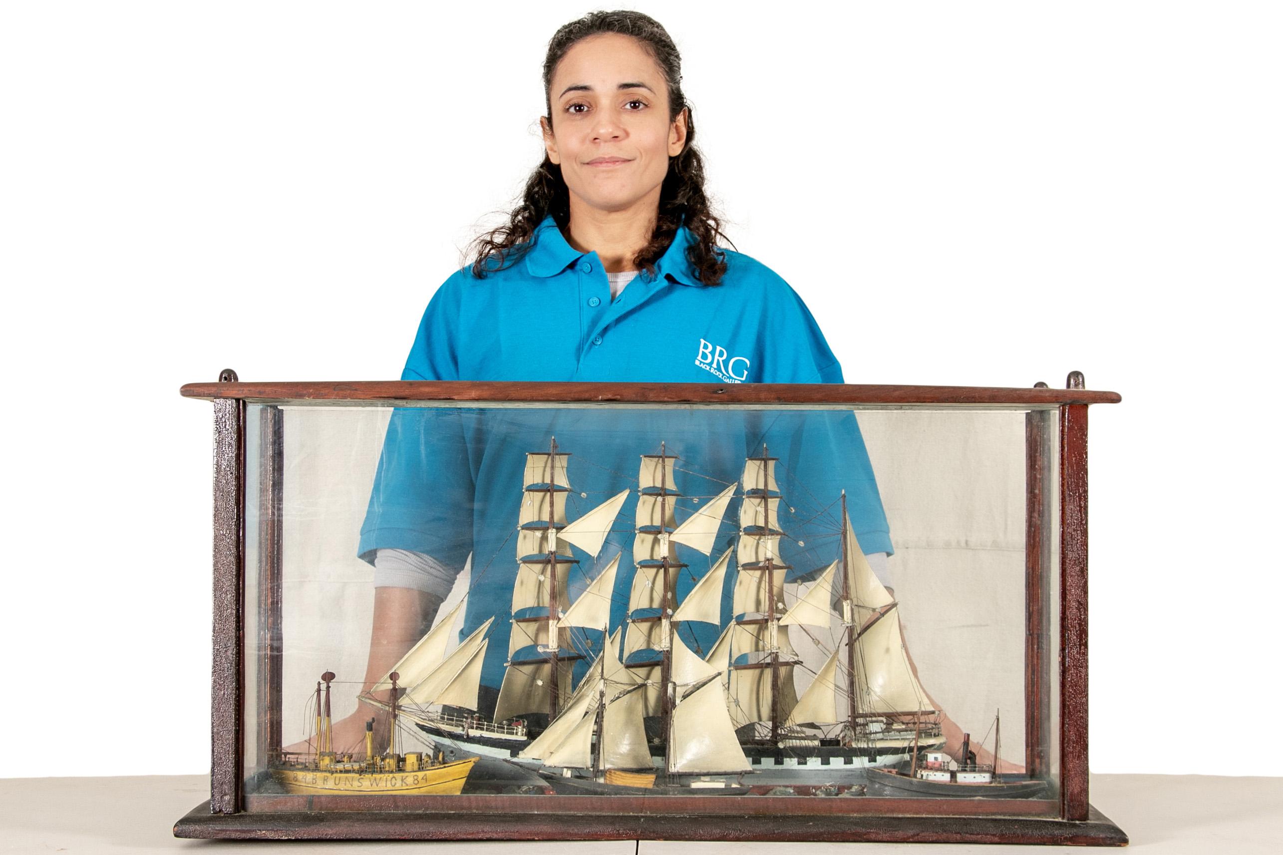 Un impressionnant et inhabituel diorama de navire du 19e siècle en coffrage, présentant quatre navires en mer. Une goélette à quatre mâts se trouve à l'arrière-plan, tandis qu'un remorqueur, un navire à deux mâts et un bateau à vapeur étiqueté 