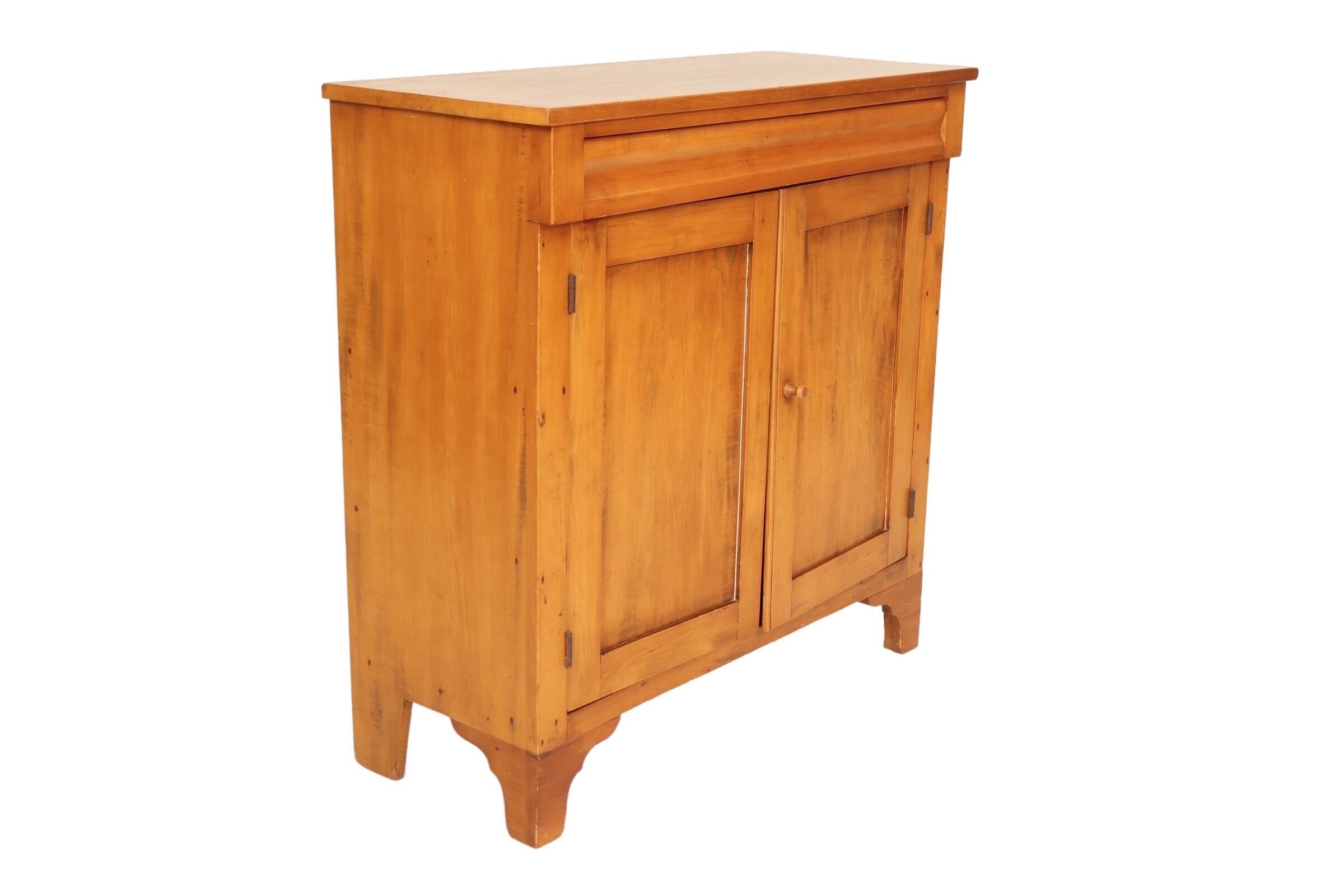 A Shaker style buffet made of cherry wood, dating from the 1860’s. Simple and utilitarian with a single hand dovetailed drawer above cabinet doors that house two shelves. The drawer pulls open from underneath with an undulating beveled drawer front.