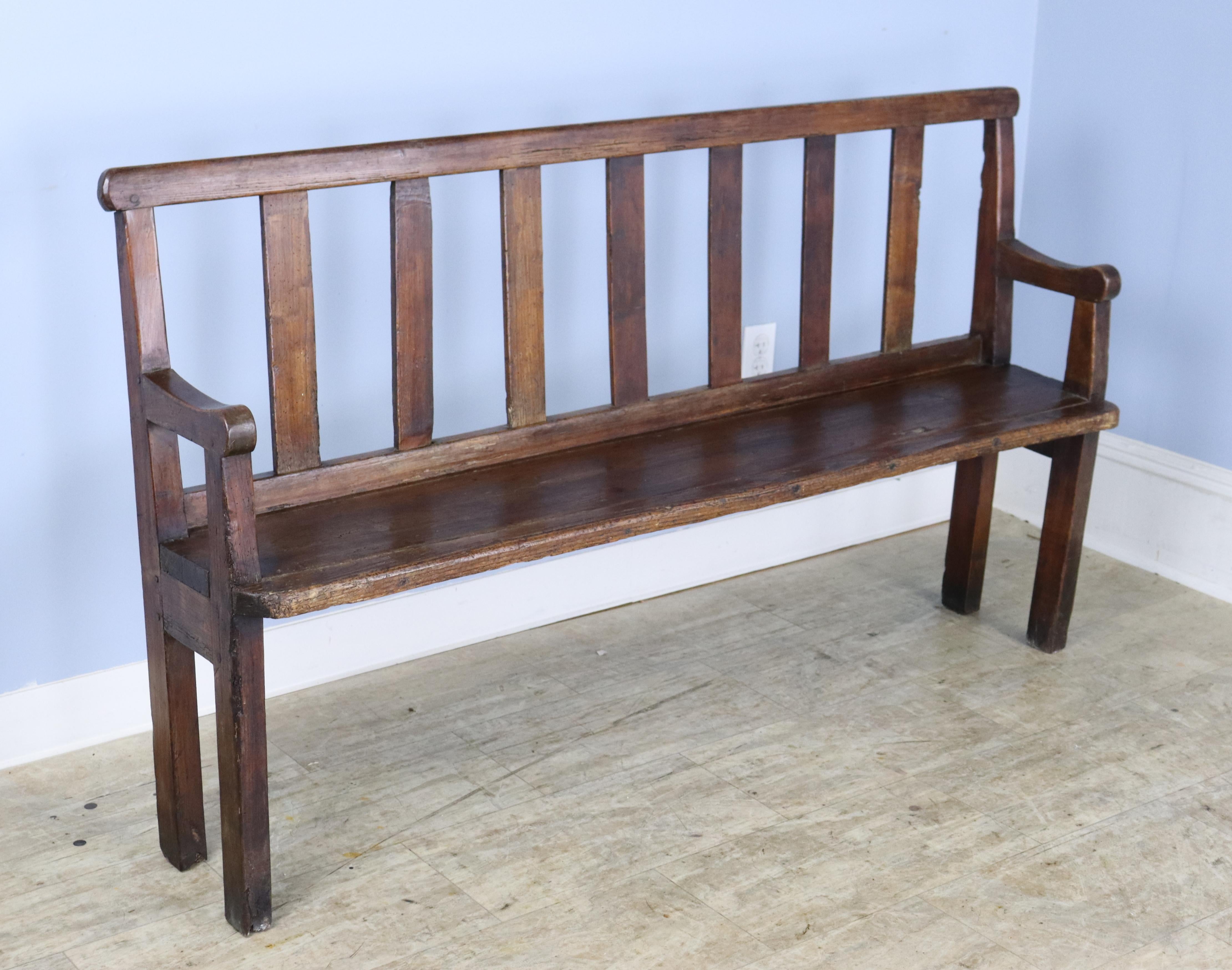A slim country bench with eye catching back supports and some interesting age appropriate wear, shown.  The piece is shallow for a small entrance hall, at the end of the bed, or in a small vestibule.