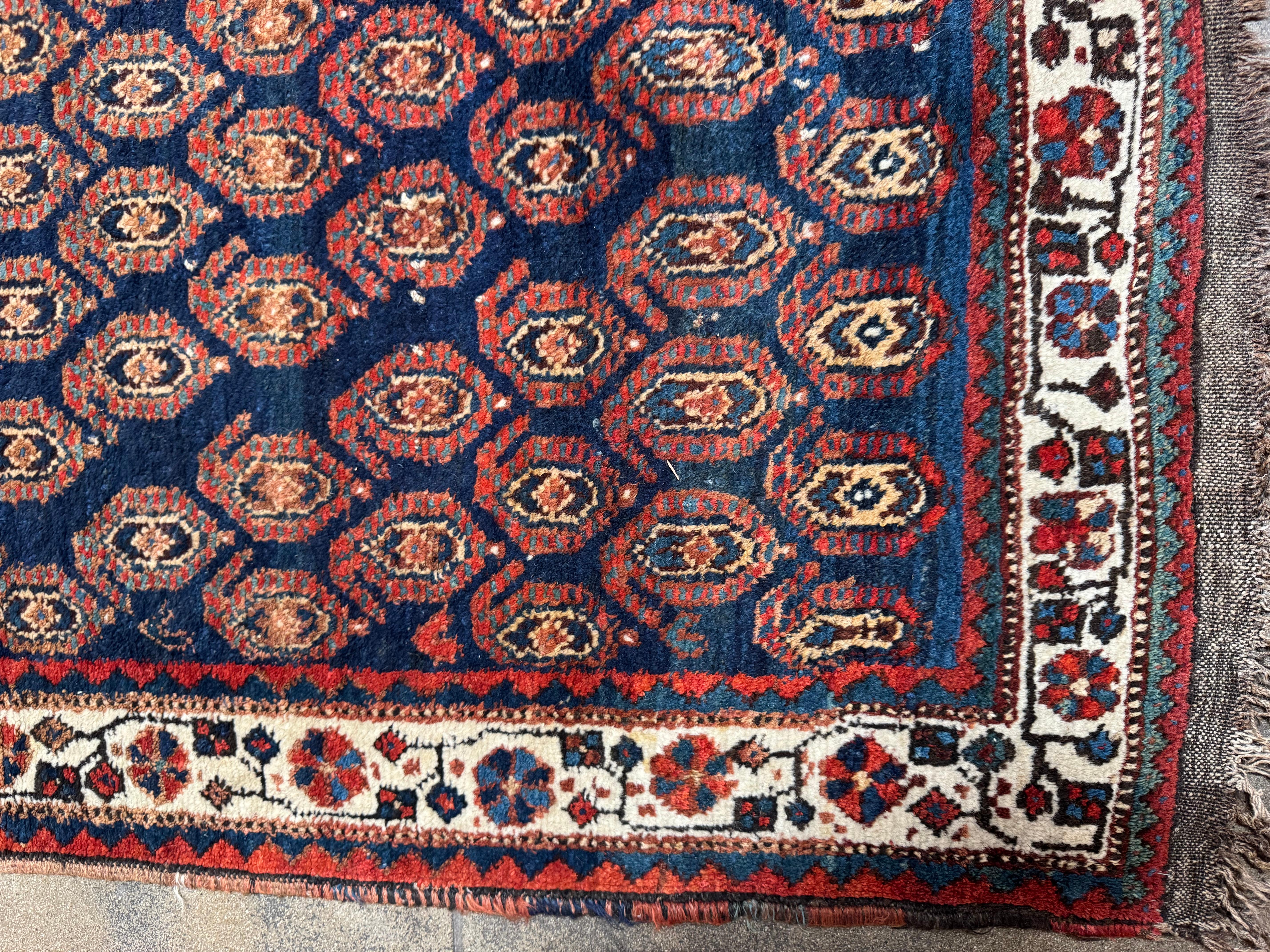 This antique Sheeraz tribal rug features a captivating field of repeating gul motifs, each framed within octagonal medallions that showcase the geometric precision and cultural richness of traditional Persian tribal weaving. The deep navy and