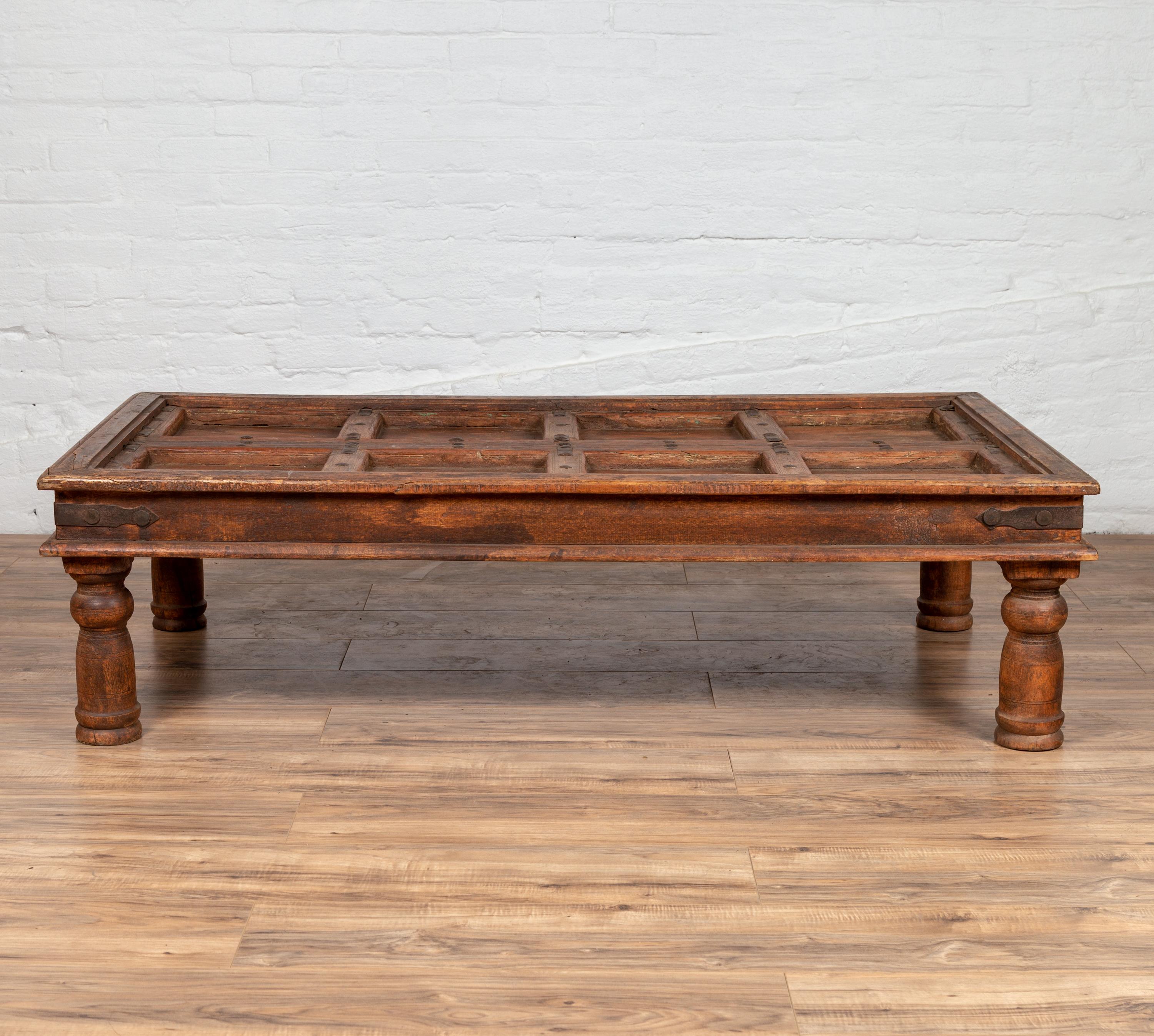 An antique Indian palace door made into a coffee table with sheesham wood and iron studs. Born in India during the early years of the 20th century, this charming palace door has been made into a coffee table. The top, presenting a succession of