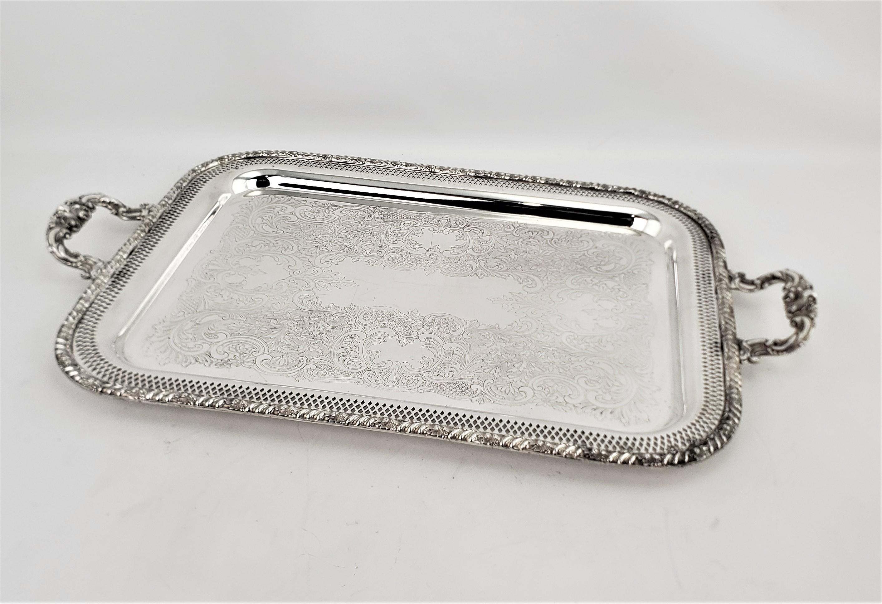 This large antique silver plated serving tray is signed by an unknown maker and presumed to have originated from England and dating to approximately 1920 and done in a Victorian style. The outside rim is decorated with a leaf and flower motif and