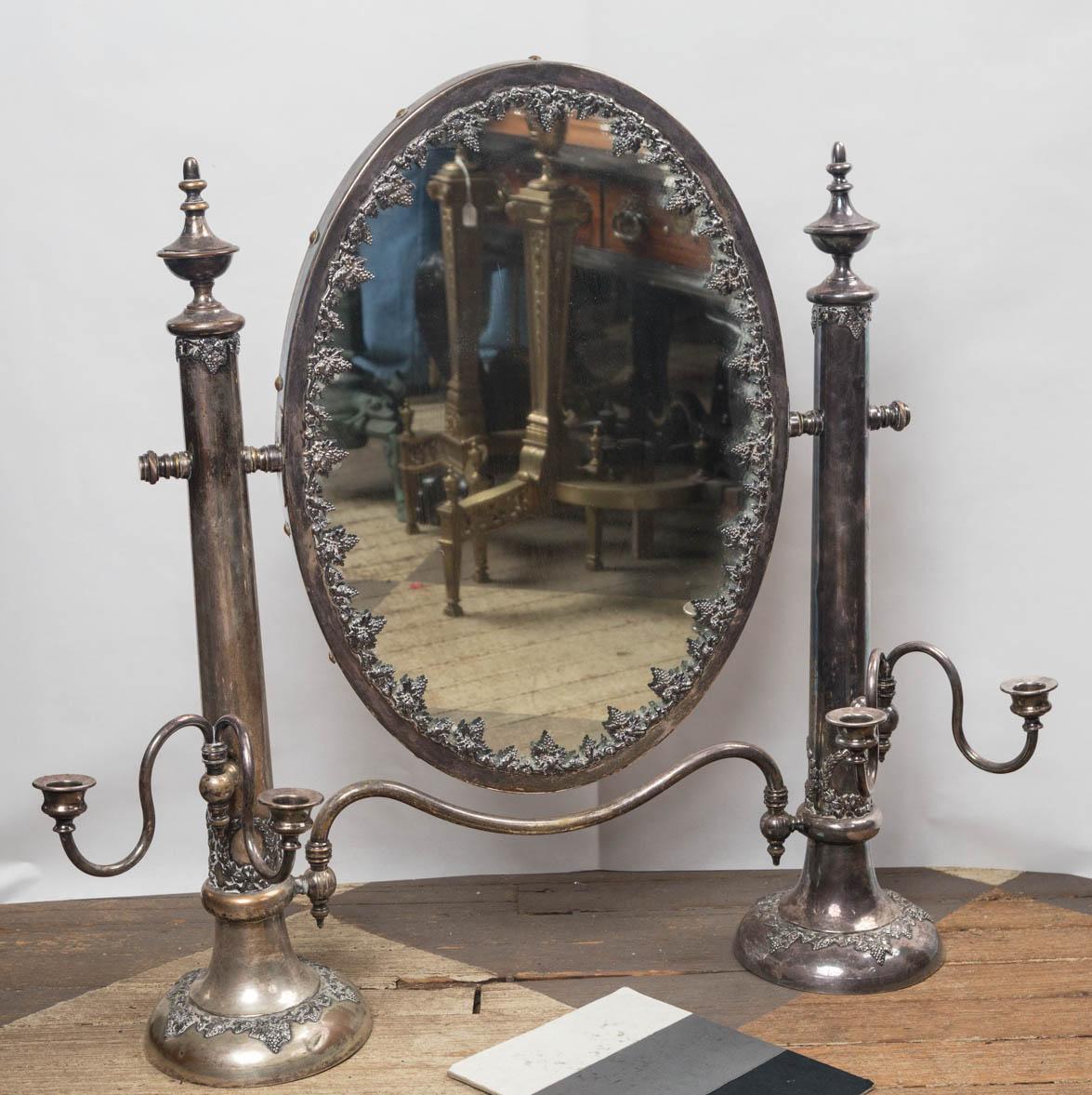 The mirror has a wooden back. The glass pivots up and down. The glass is framed with grape leaves and grapes. Two round columns attached left and right. The have urn form finials and are decorated with grape leaves and grapes. Double candle arms,